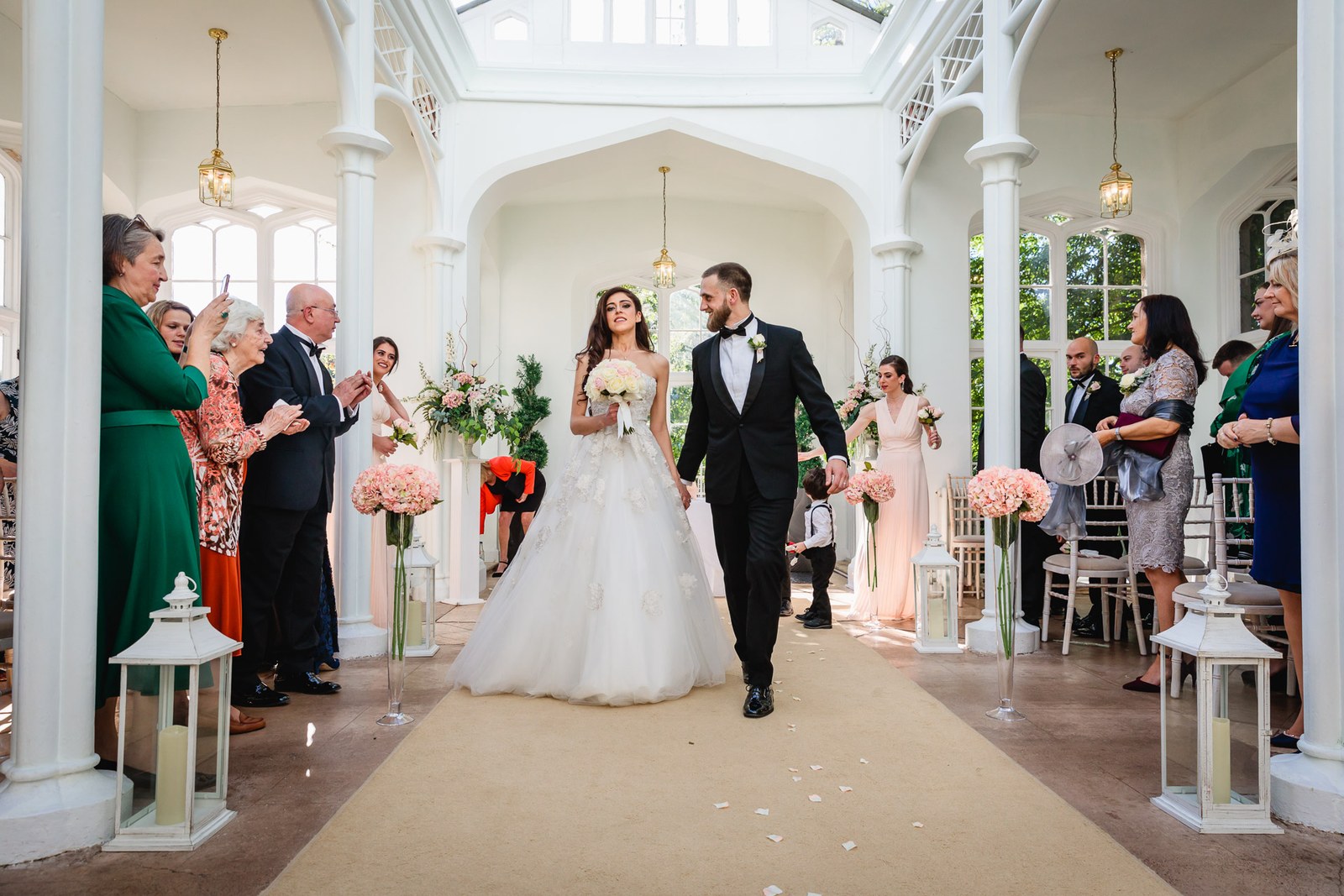 Newlyweds walk back down the orangery aisle as guests applaud at St Audries Park