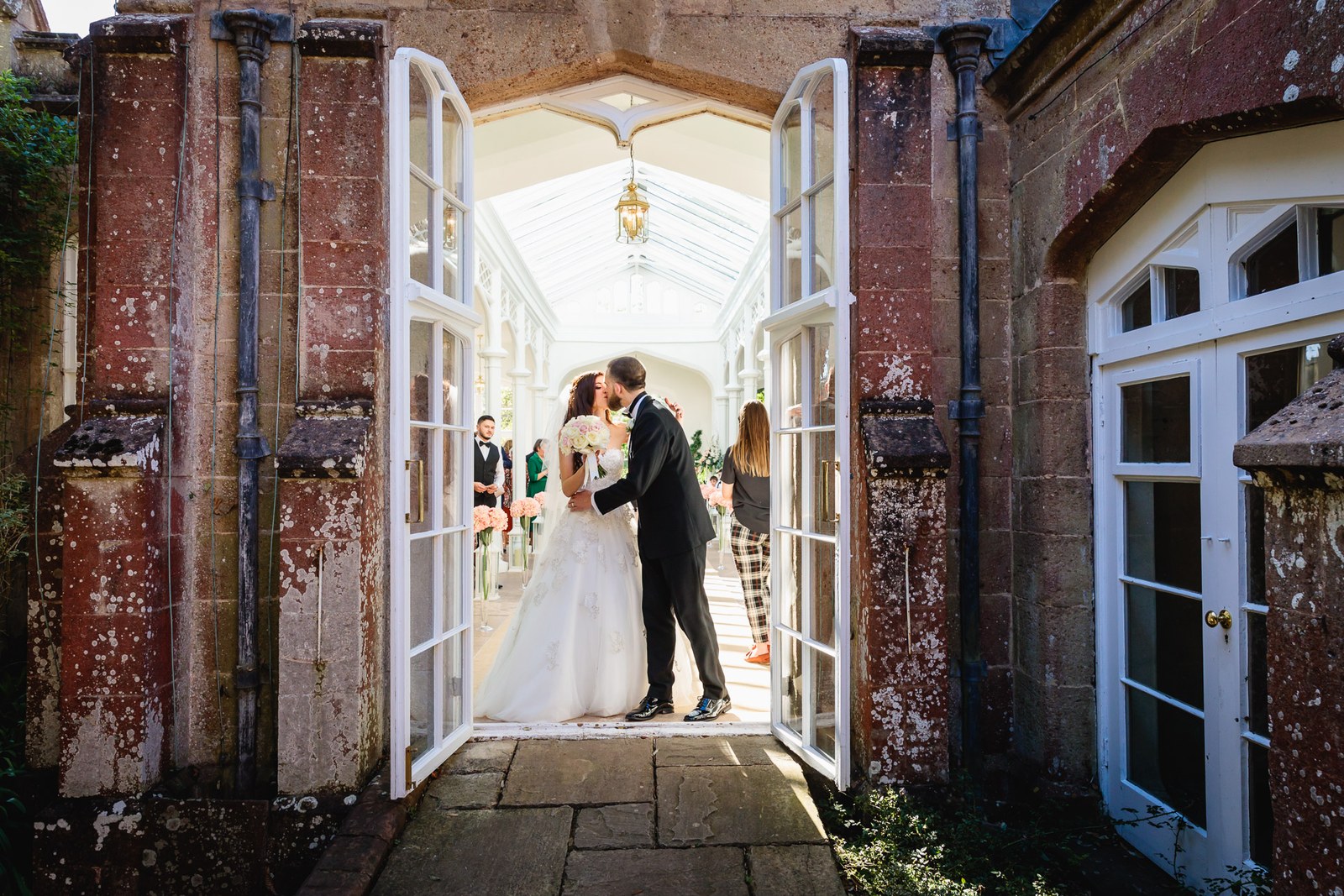 The couple kiss framed in the open stone doors of the St Audries Park orangery