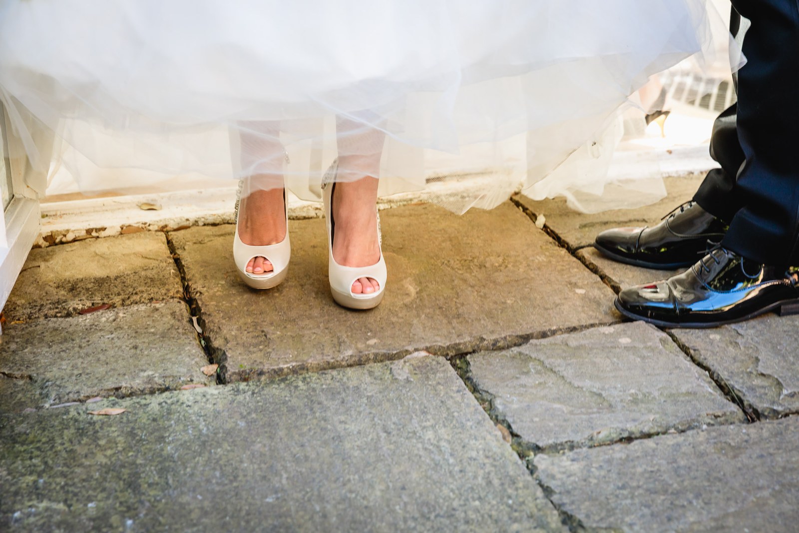 The bride's peep-toe shoes beneath her gown on weathered flagstones