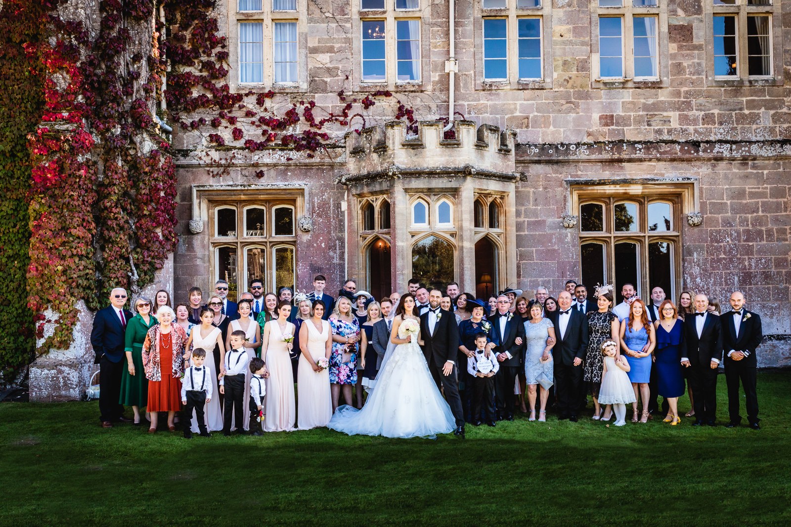 Full wedding party before the ivy-covered frontage of St Audries Park