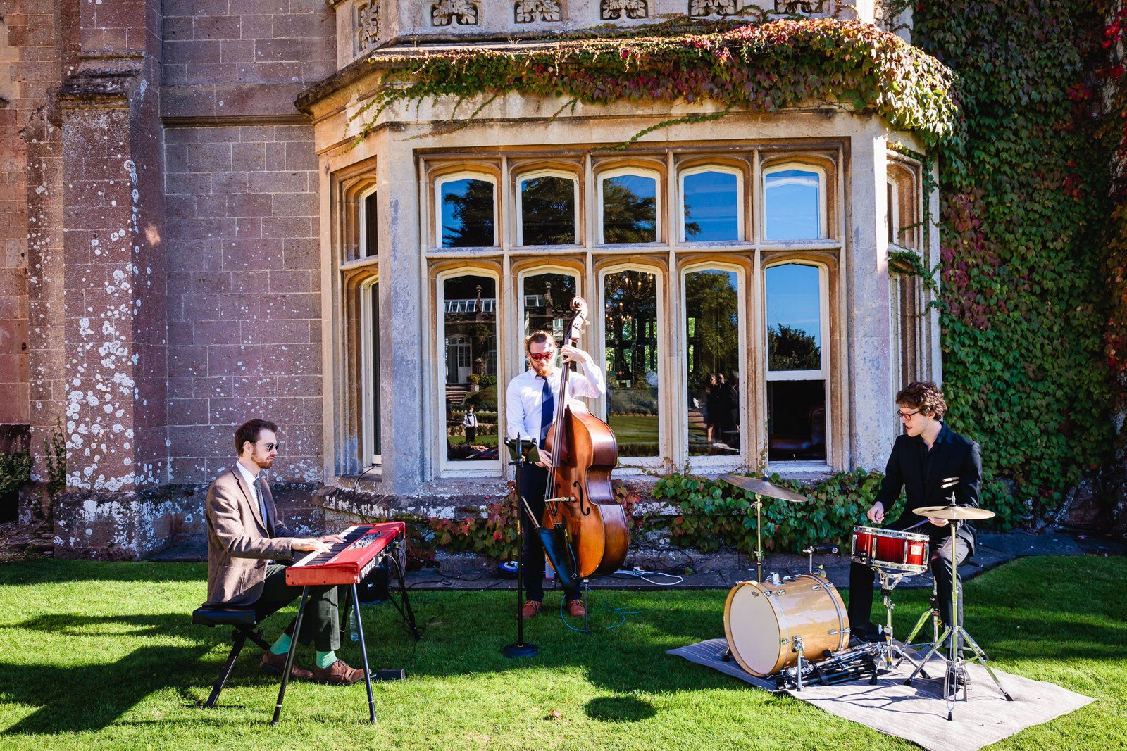 A jazz trio plays on the lawn beneath the carved bay window of St Audries Park