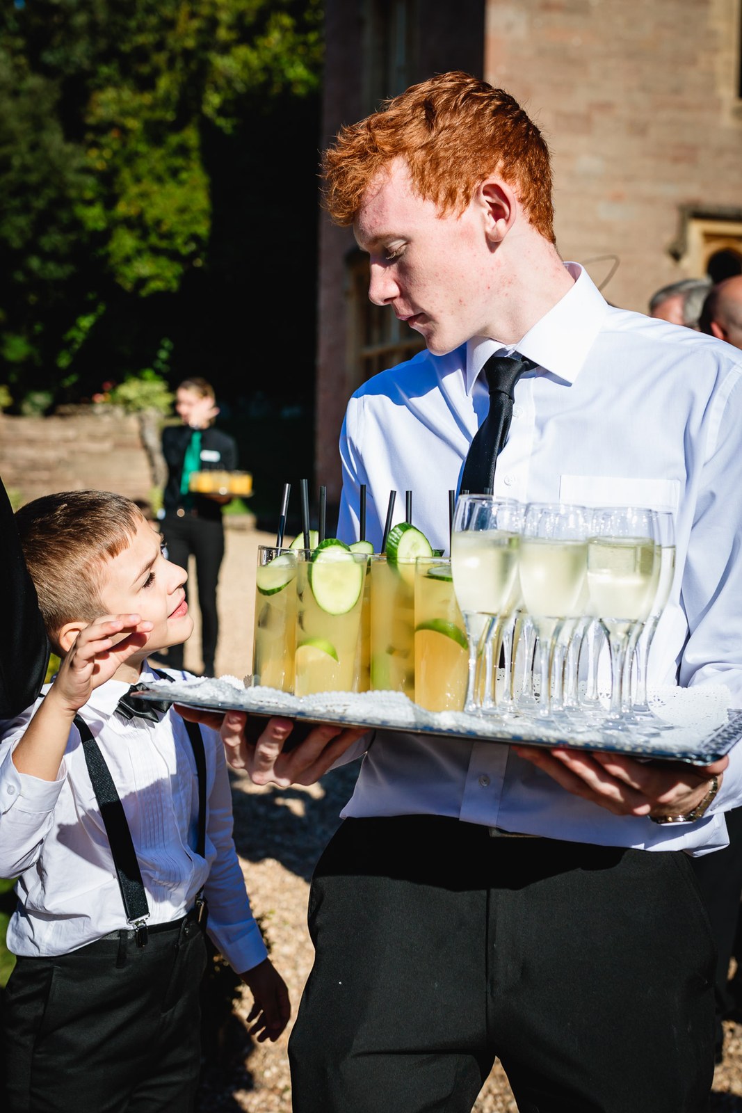 A waiter carries a tray of iced drinks past a curious page boy