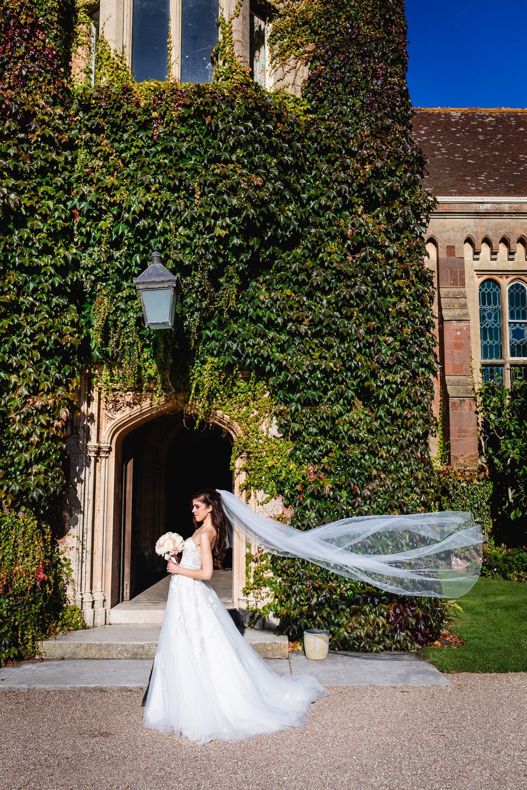 Bride before an ivy-framed arched doorway at St Audries Park, veil sweeping the stone