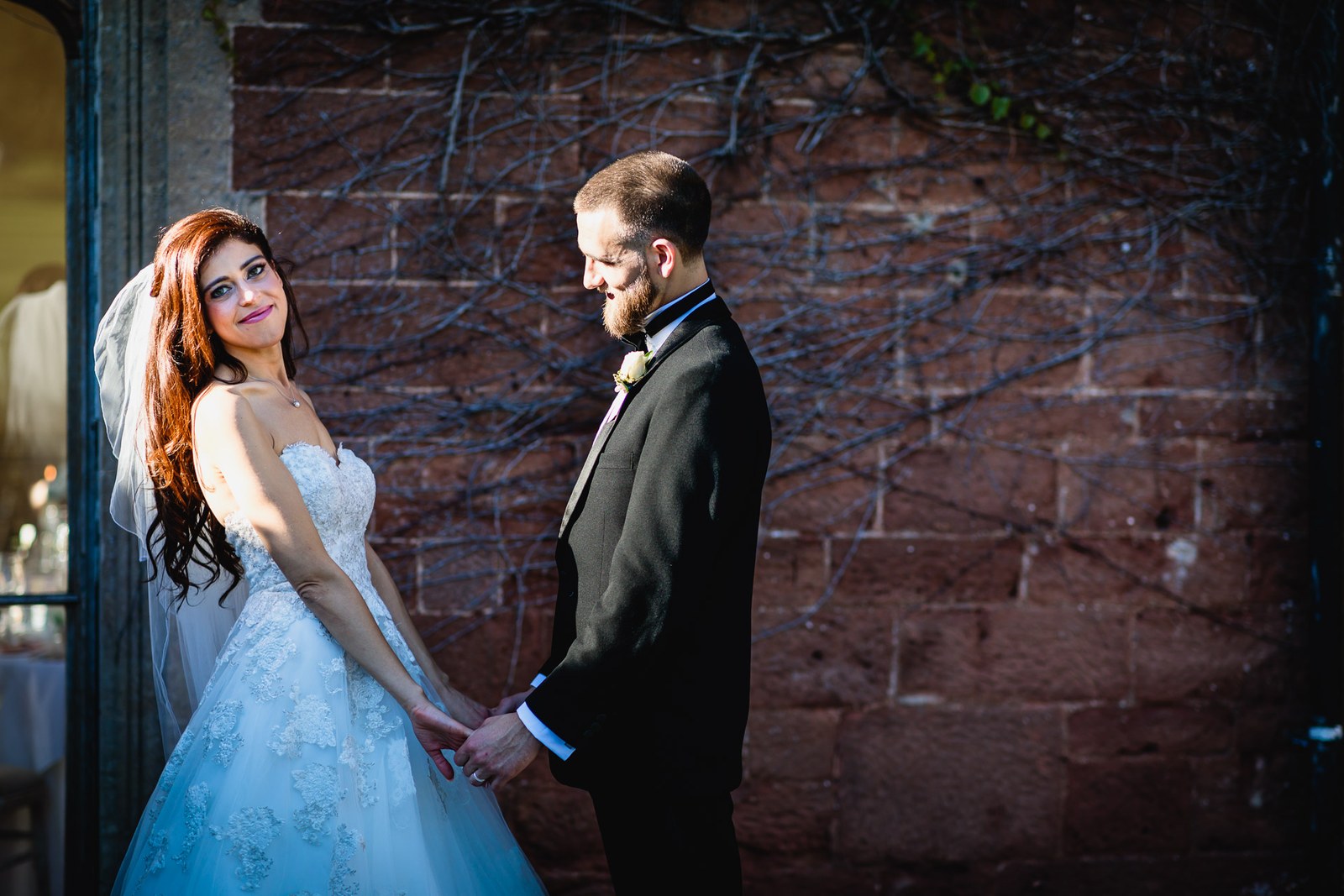 Bride and groom hold hands beside the red-stone garden wall