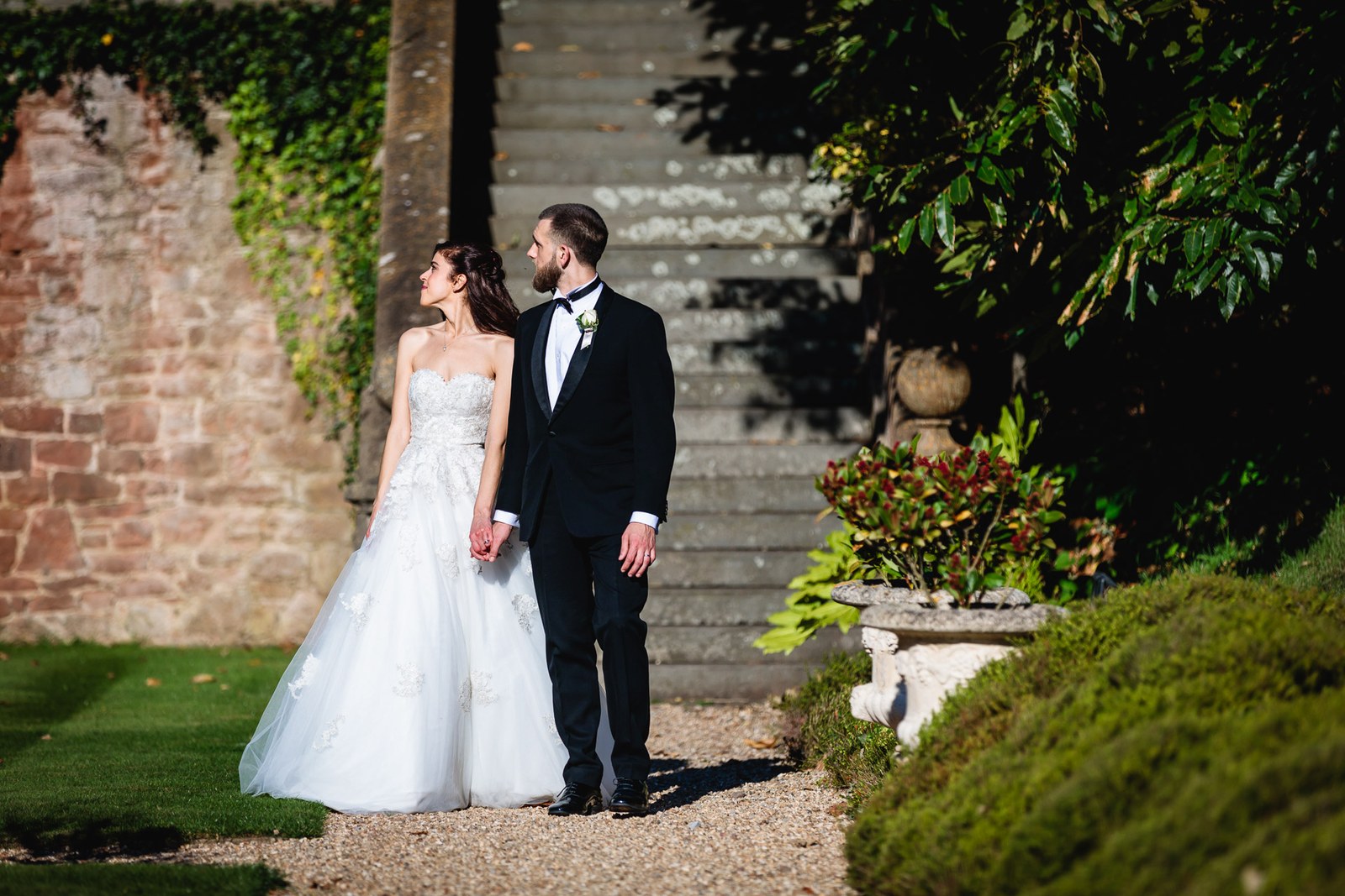 The newlyweds hold hands against the ivy-draped stone of the manor