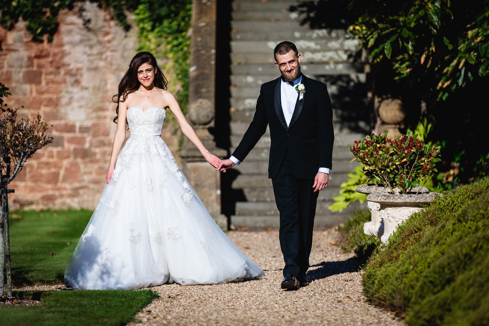 The couple walk hand in hand along the gravel path by the ivy-clad wall