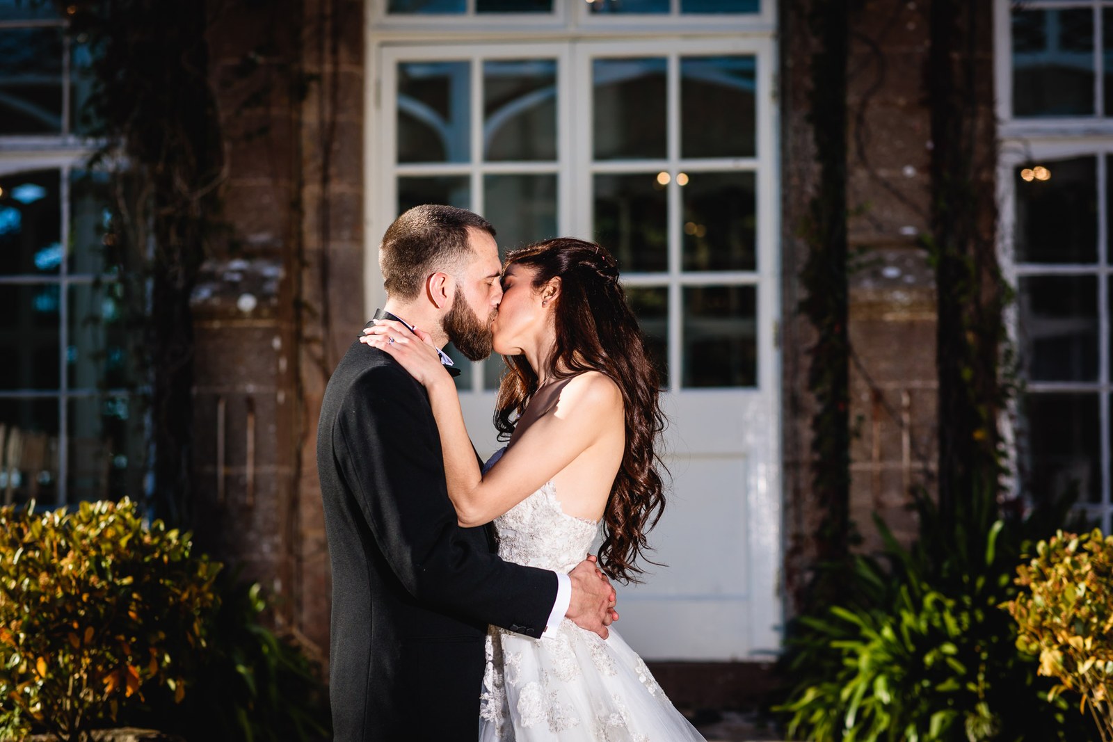 Bride and groom kiss before the white French doors of the orangery
