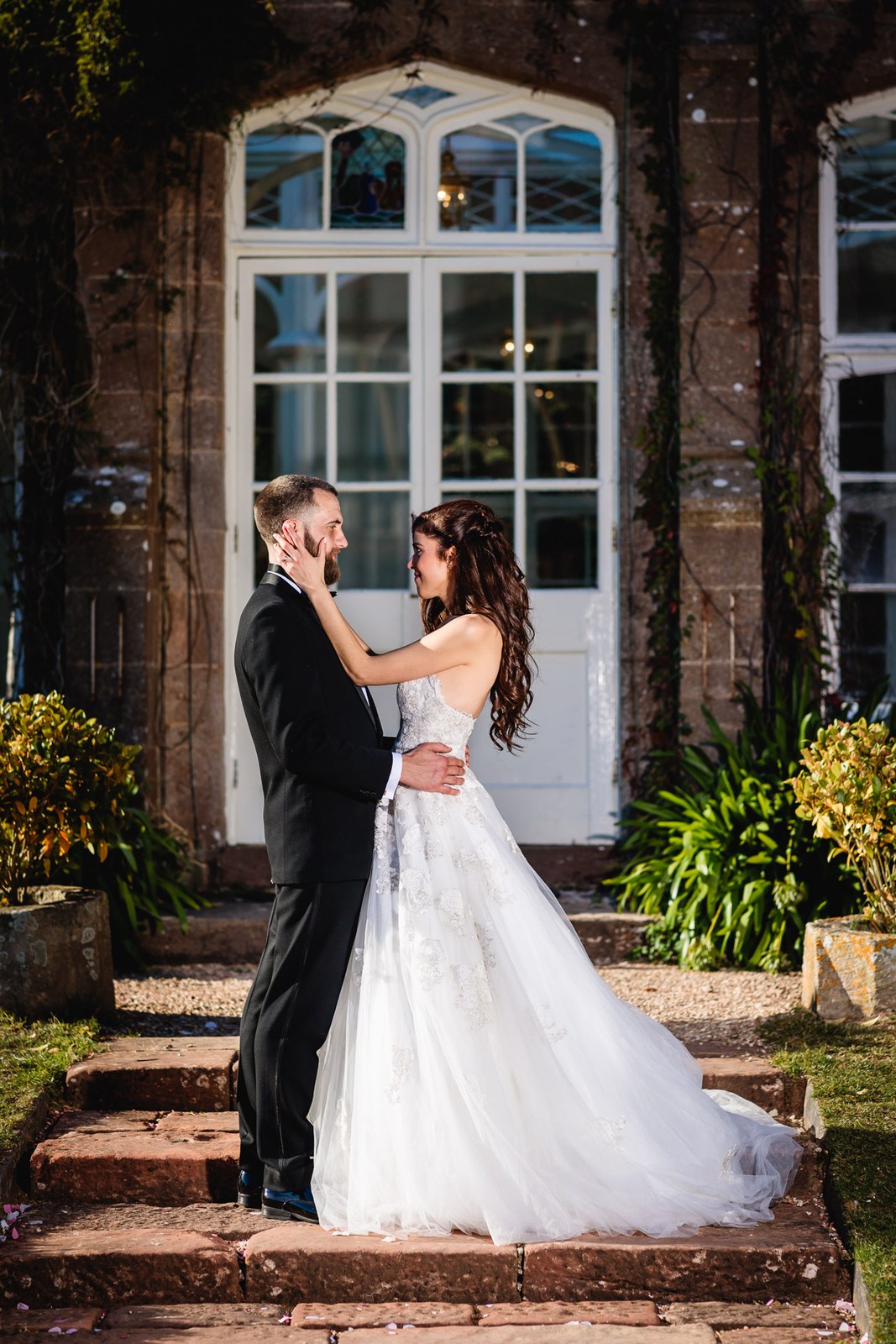 Bride and groom face each other framed by the orangery's arched glass doors