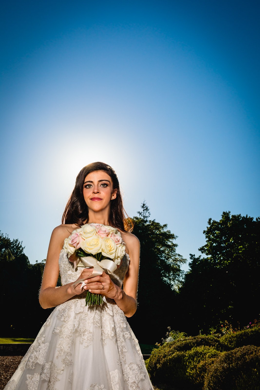 Backlit portrait of the bride holding her rose bouquet against blue sky