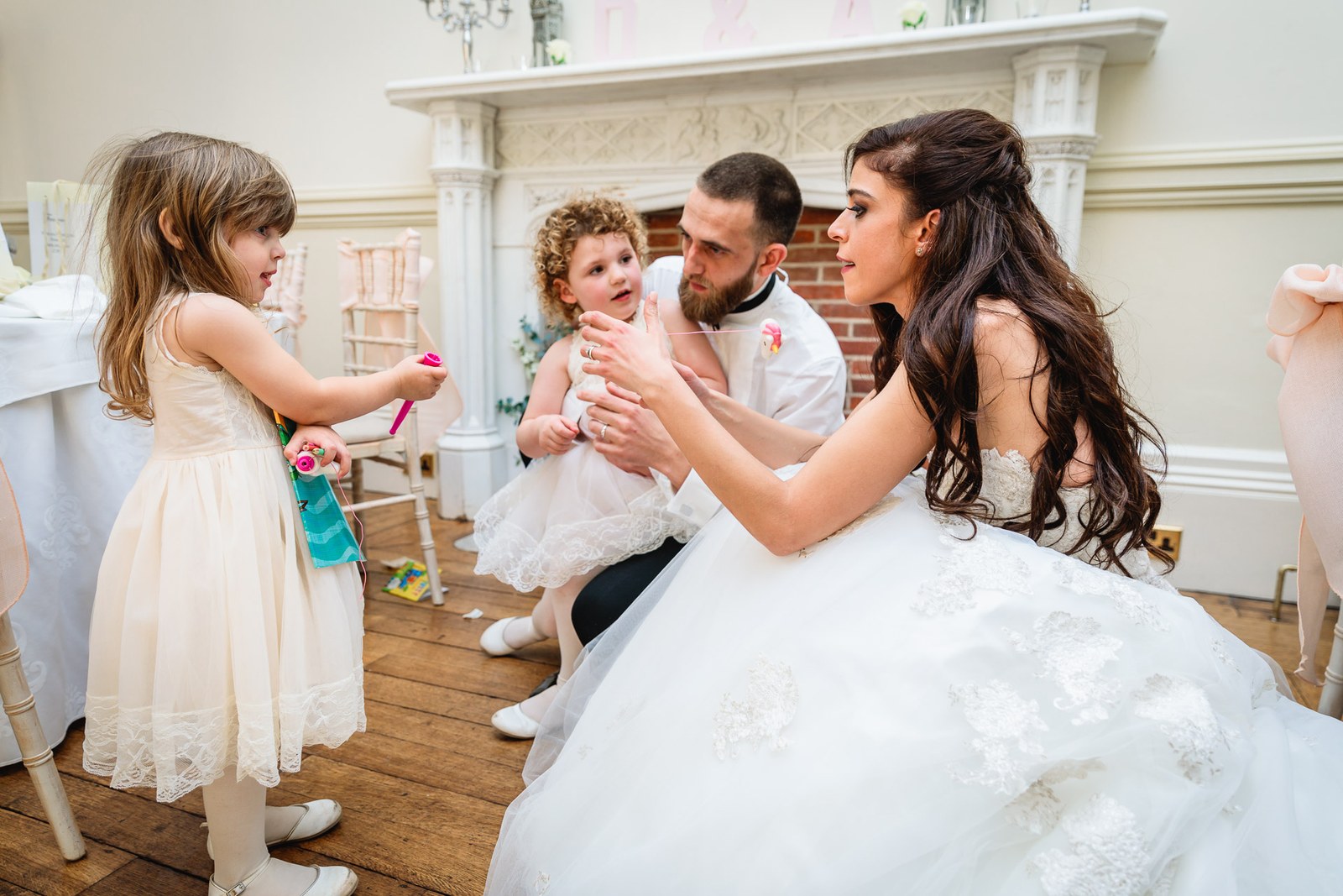 Bride and groom play with the flower girls beside the marble fireplace