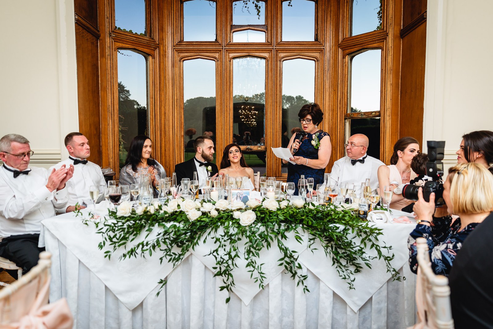 A woman gives a speech at the top table dressed with a greenery garland