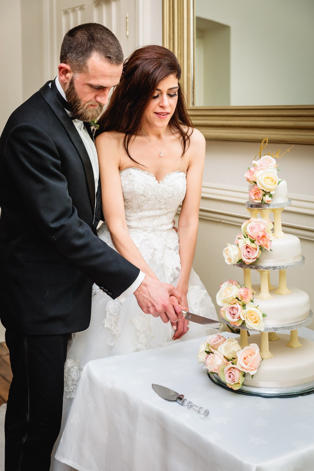 Bride and groom cut their rose-trimmed tiered cake together