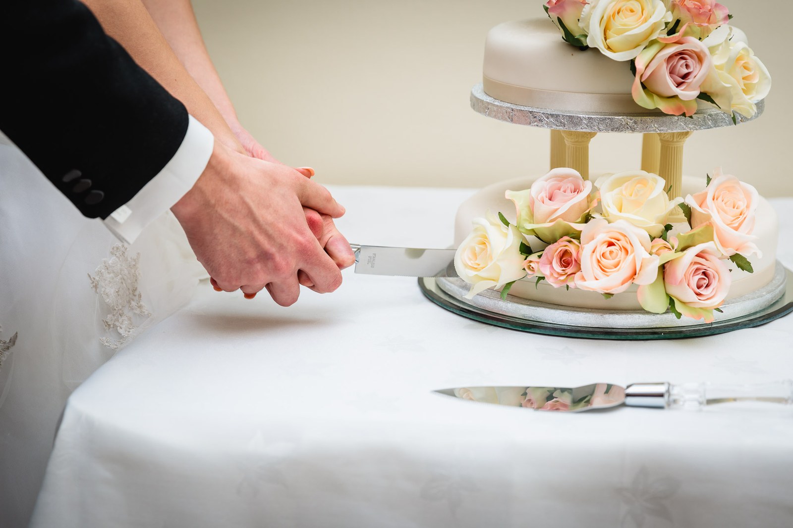 Close-up of the couple's hands on the knife amid the cake's roses