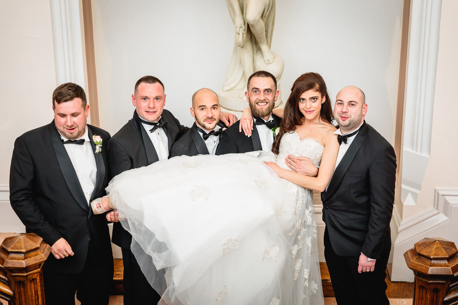Groomsmen hold the bride aloft before a marble statue