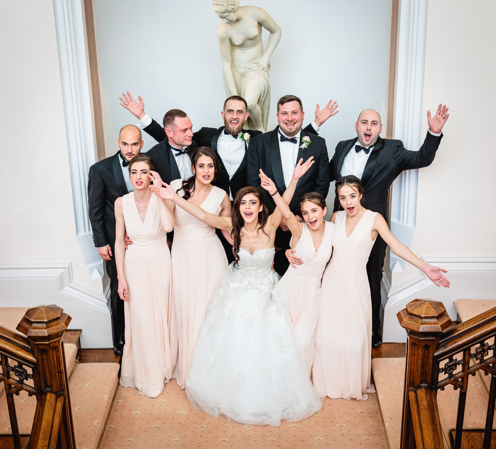 The wedding party pull playful poses on the grand staircase