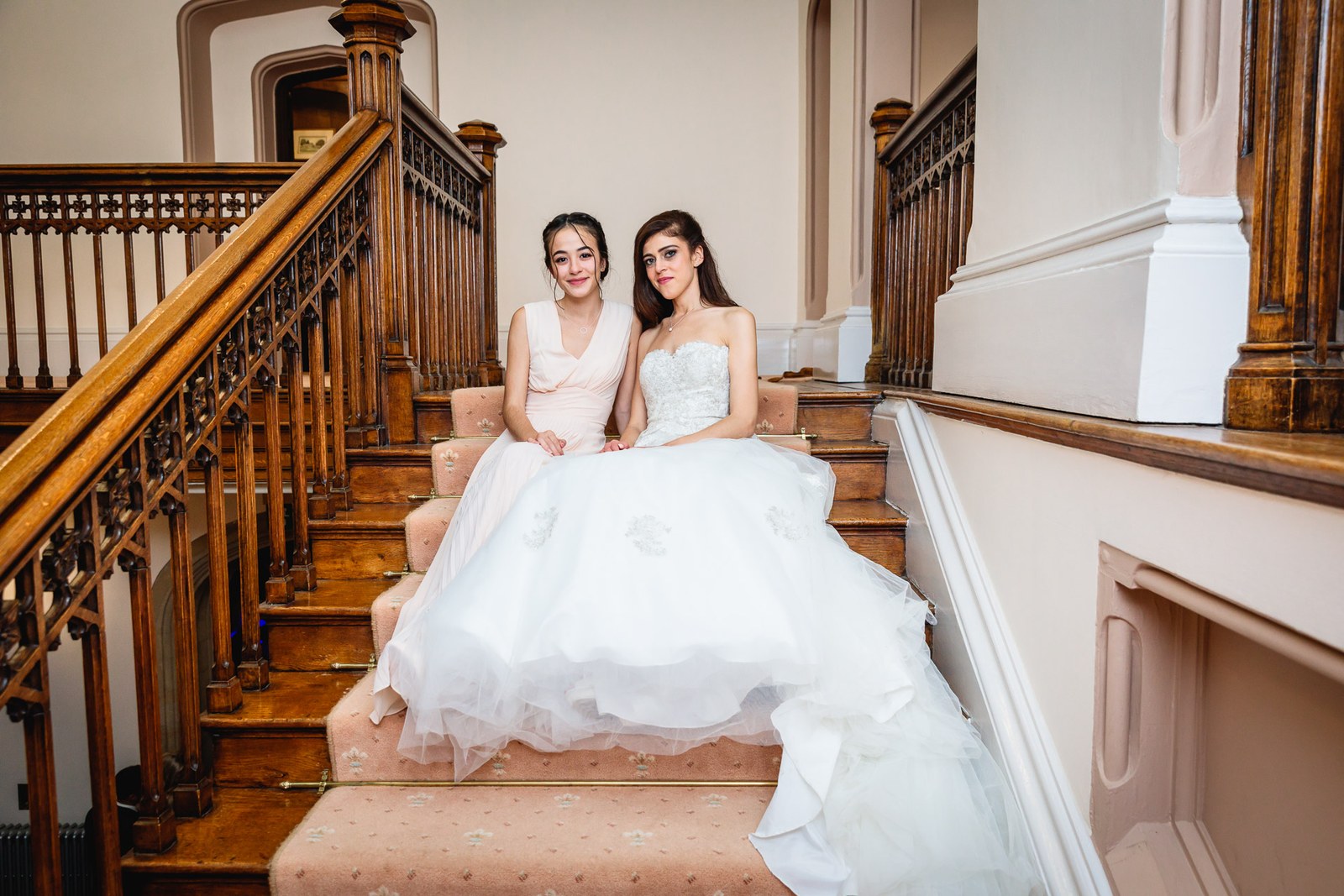 The bride seated with a bridesmaid on the carved wooden staircase