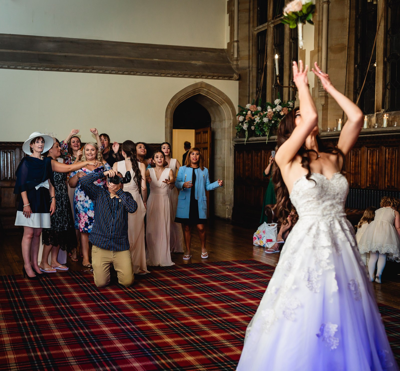 Bride tosses her bouquet to gathered guests across the tartan-carpeted hall