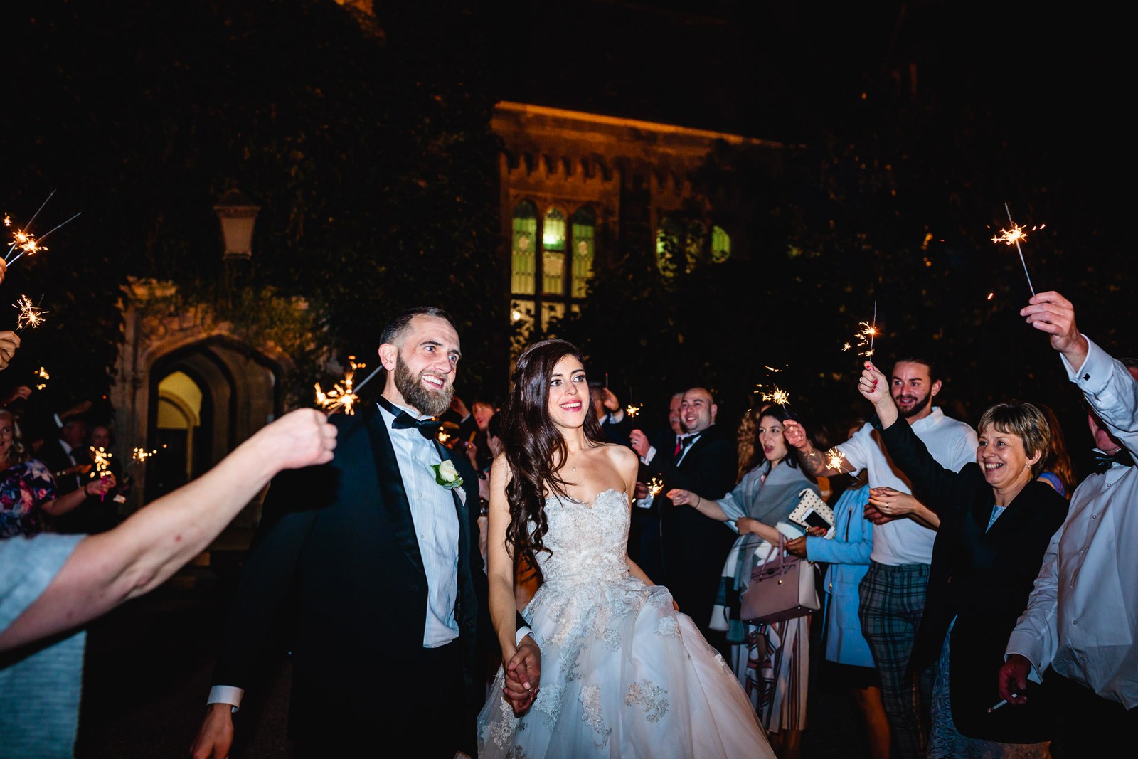 Newlyweds pass through raised sparklers held by guests in the night air