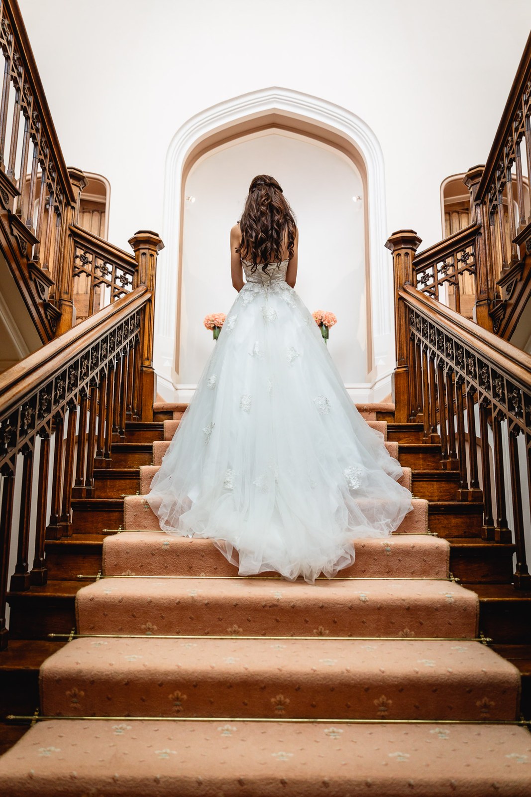 Bride climbs the grand St Audries Park staircase towards an arched window