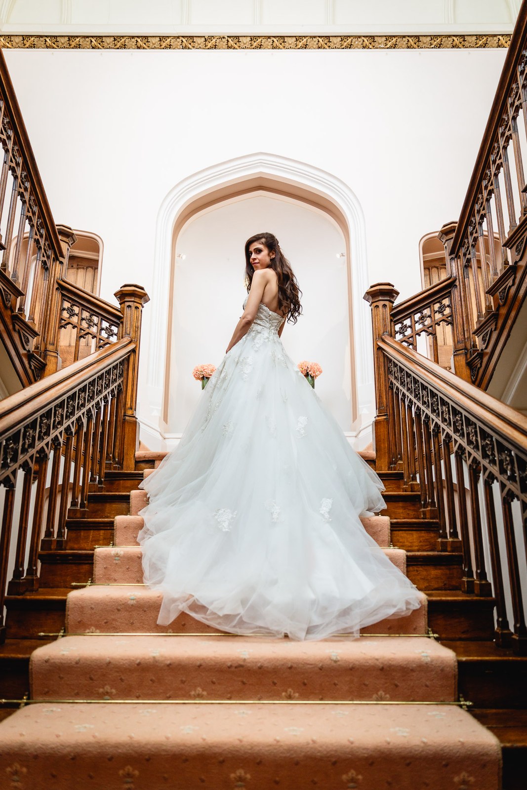Bride glances back over her shoulder on the sweeping wooden staircase