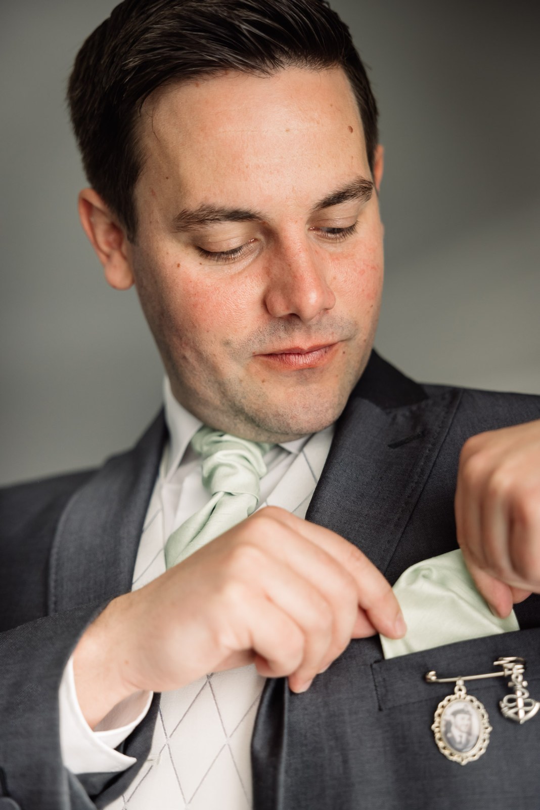 Groom in a grey suit and sage tie adjusting his pocket square before the ceremony