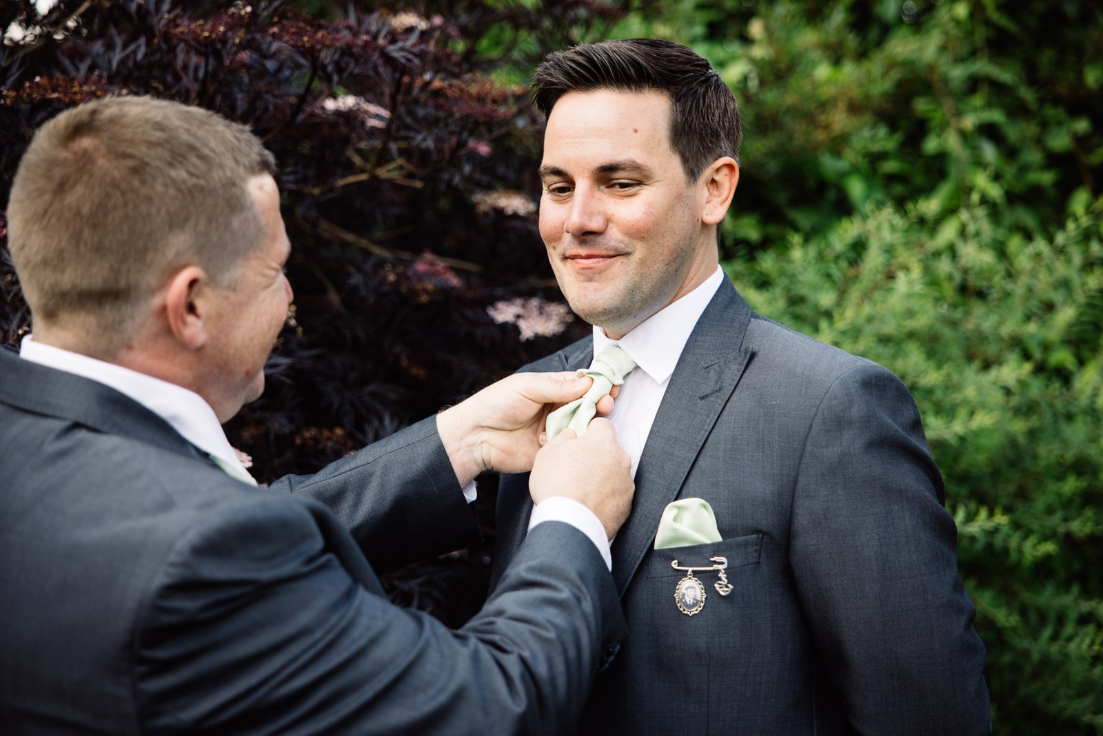 The groom's sage tie being straightened for him outside before the ceremony