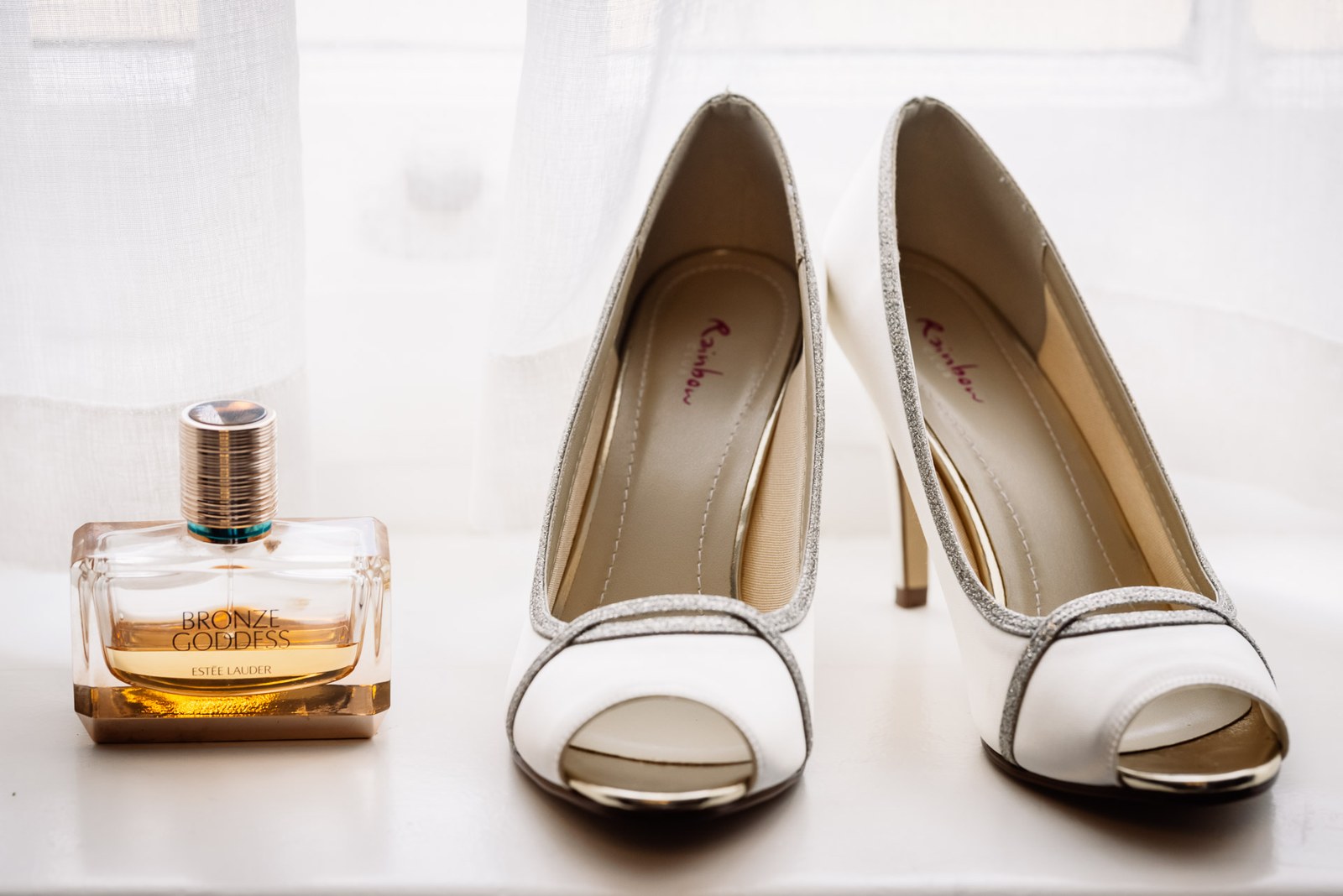 Peep-toe bridal heels beside a bottle of Estee Lauder Bronze Goddess perfume