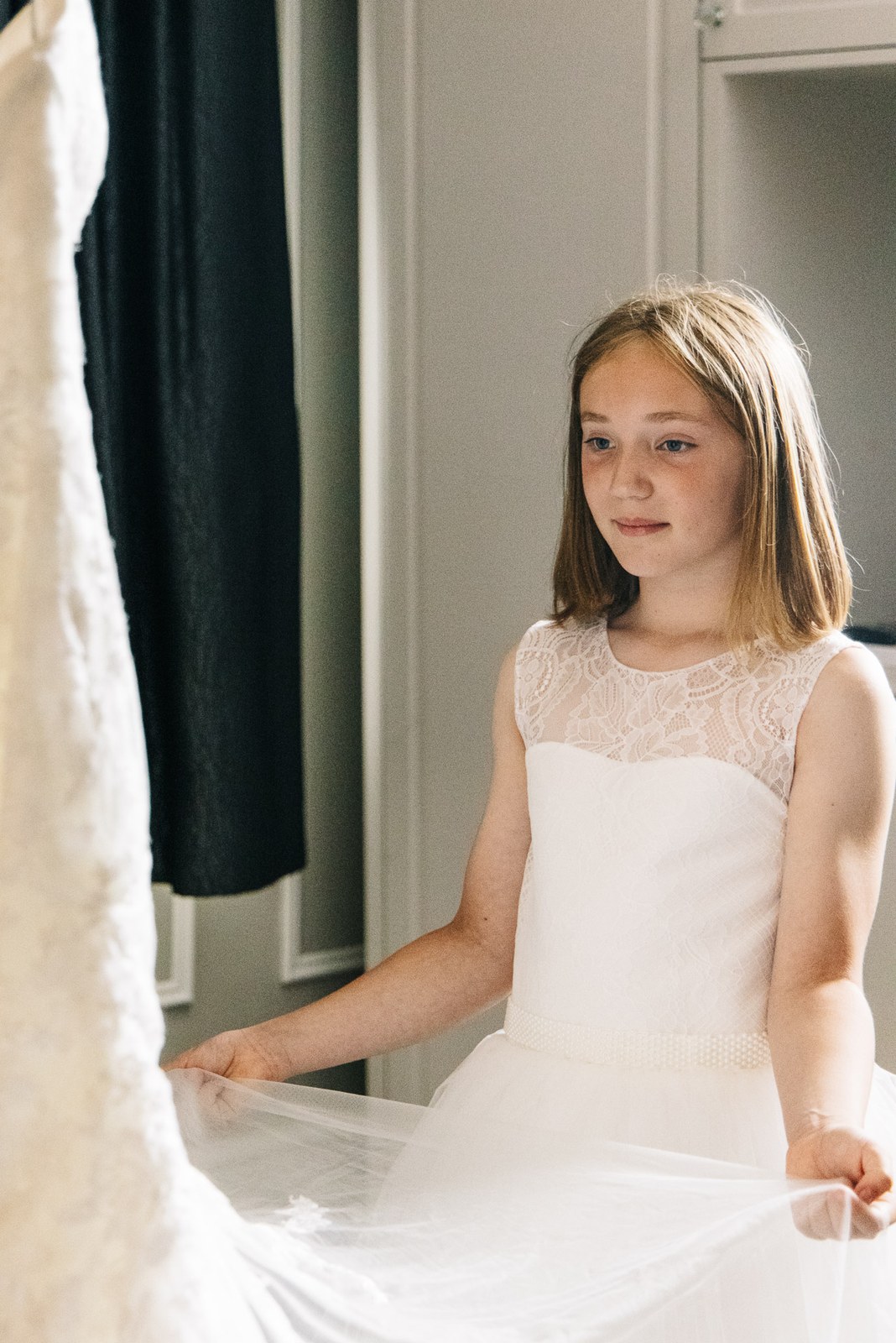 Flower girl in white holding out the bride's veil during the morning preparations