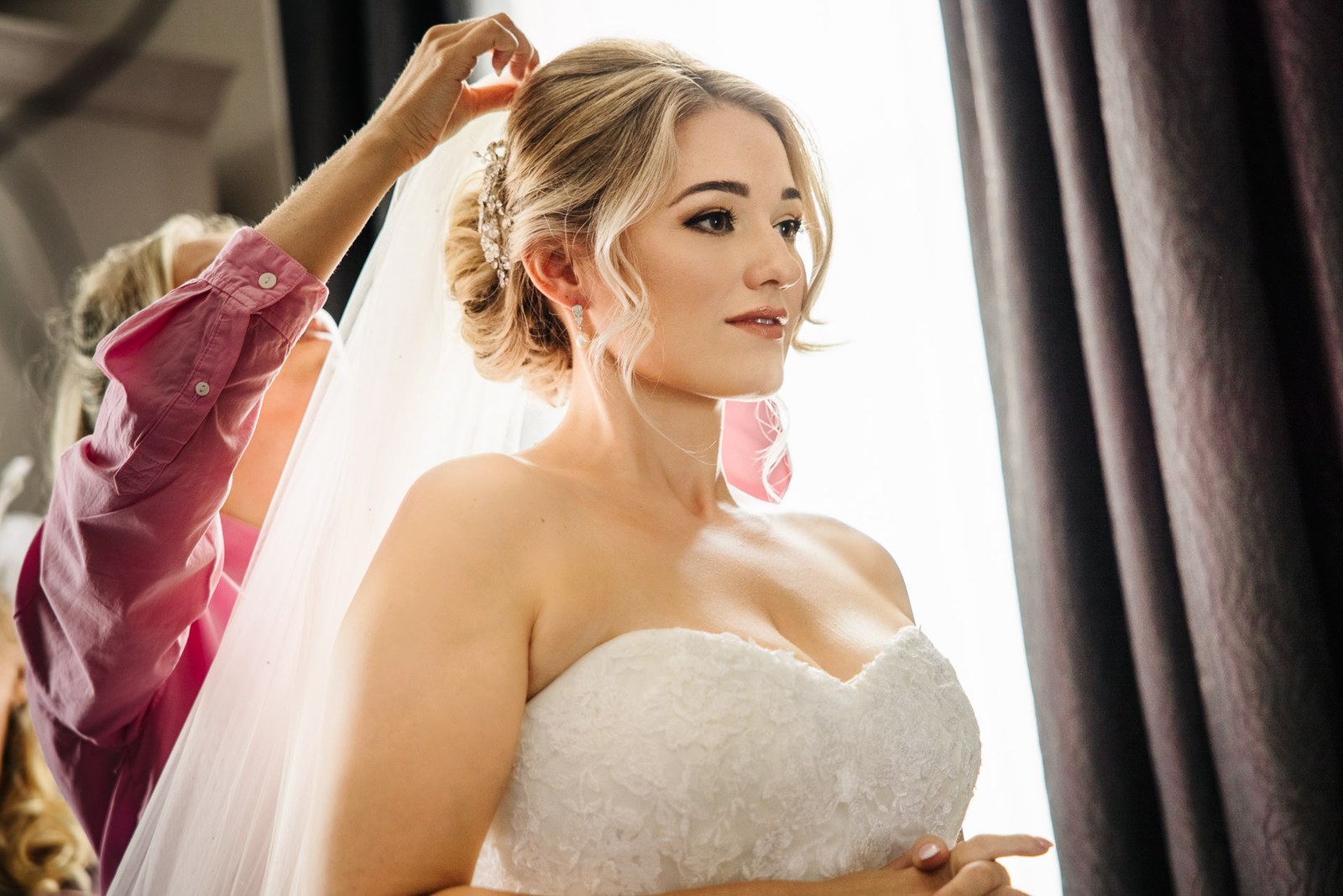 The veil being fixed into place as the bride stands in her strapless gown
