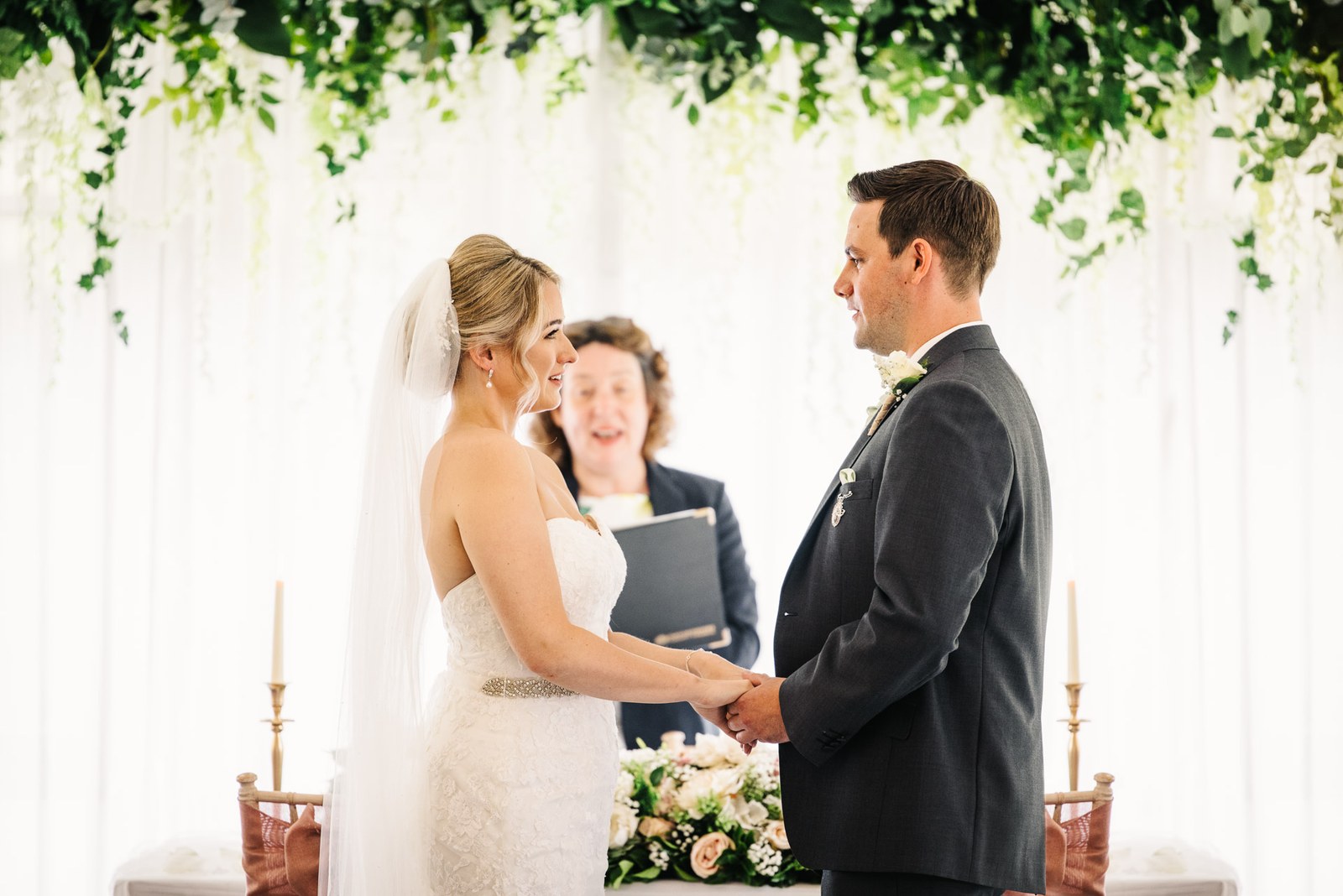 The couple holding hands and exchanging vows under the floral arch