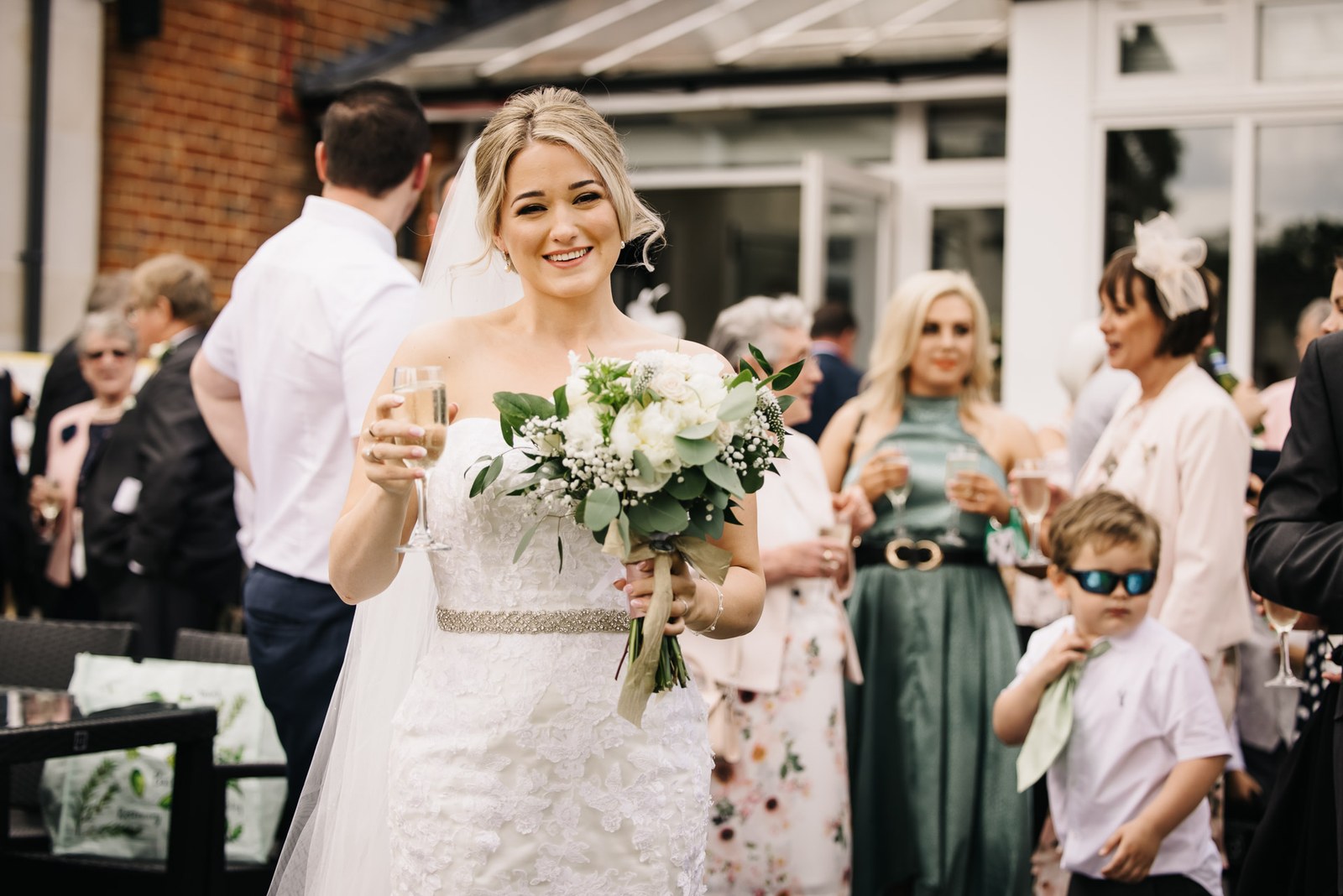 The bride with a glass of fizz among guests at the drinks reception