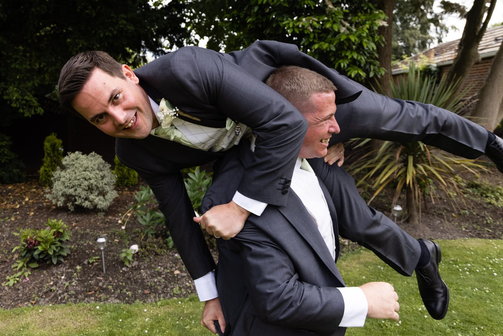 The groom hoisted horizontally by a groomsman in a playful garden moment