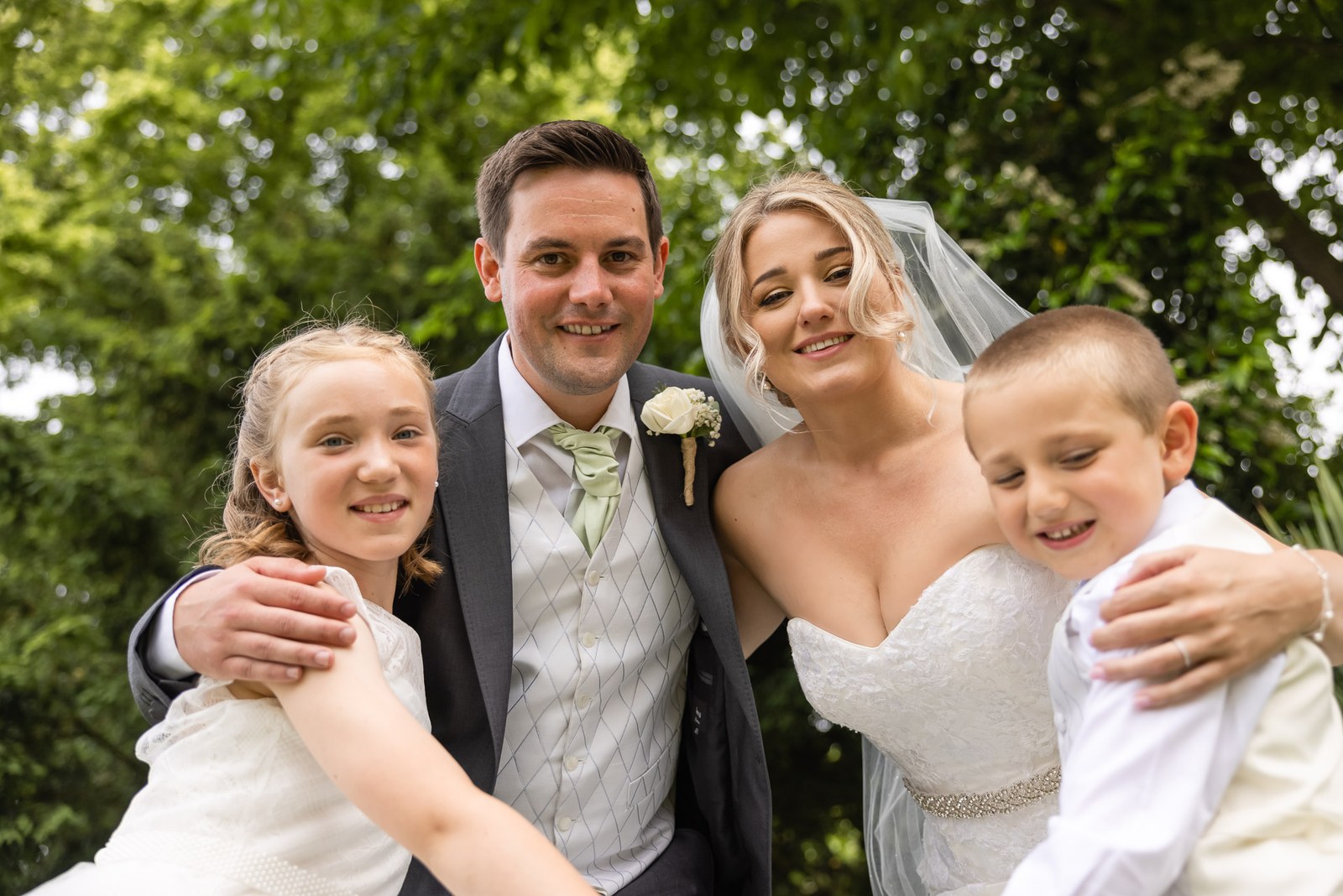 Bride, groom, flower girl and page boy sharing a group hug on the lawn