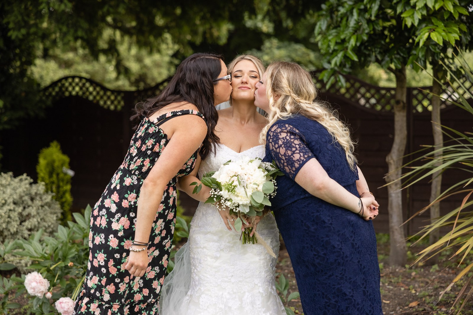 The bride kissed on both cheeks by two women in the garden