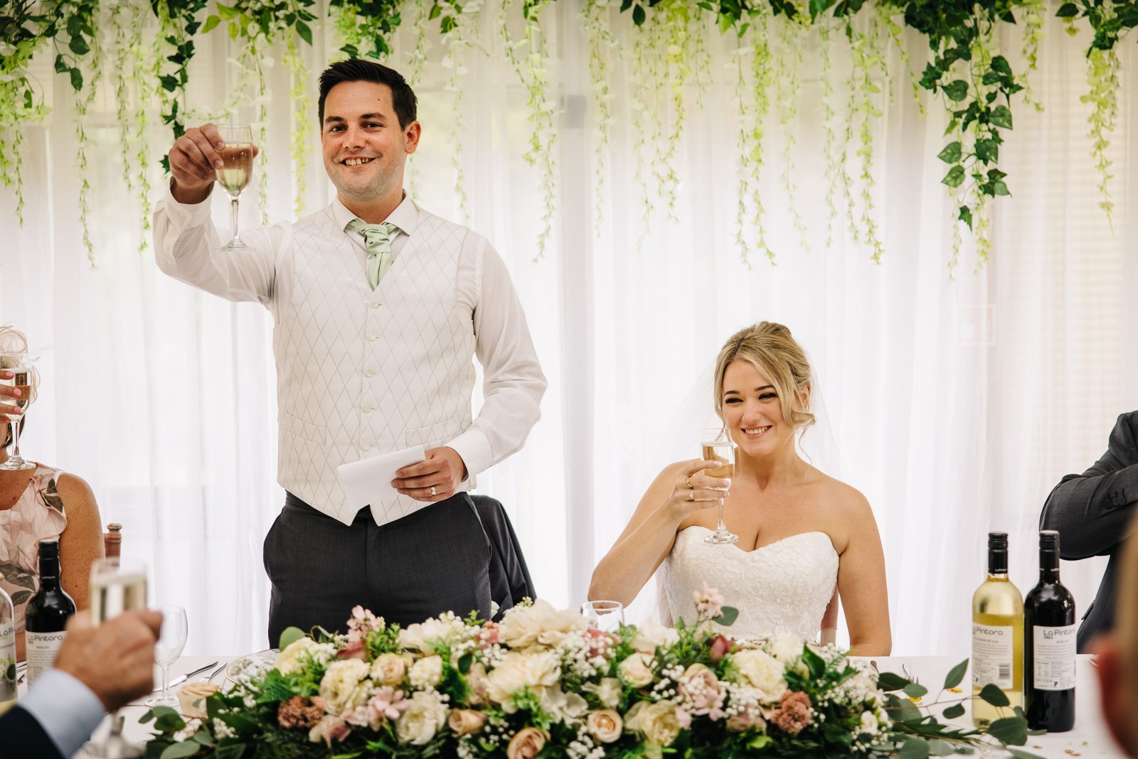 The groom raising his glass for a speech beside the seated bride