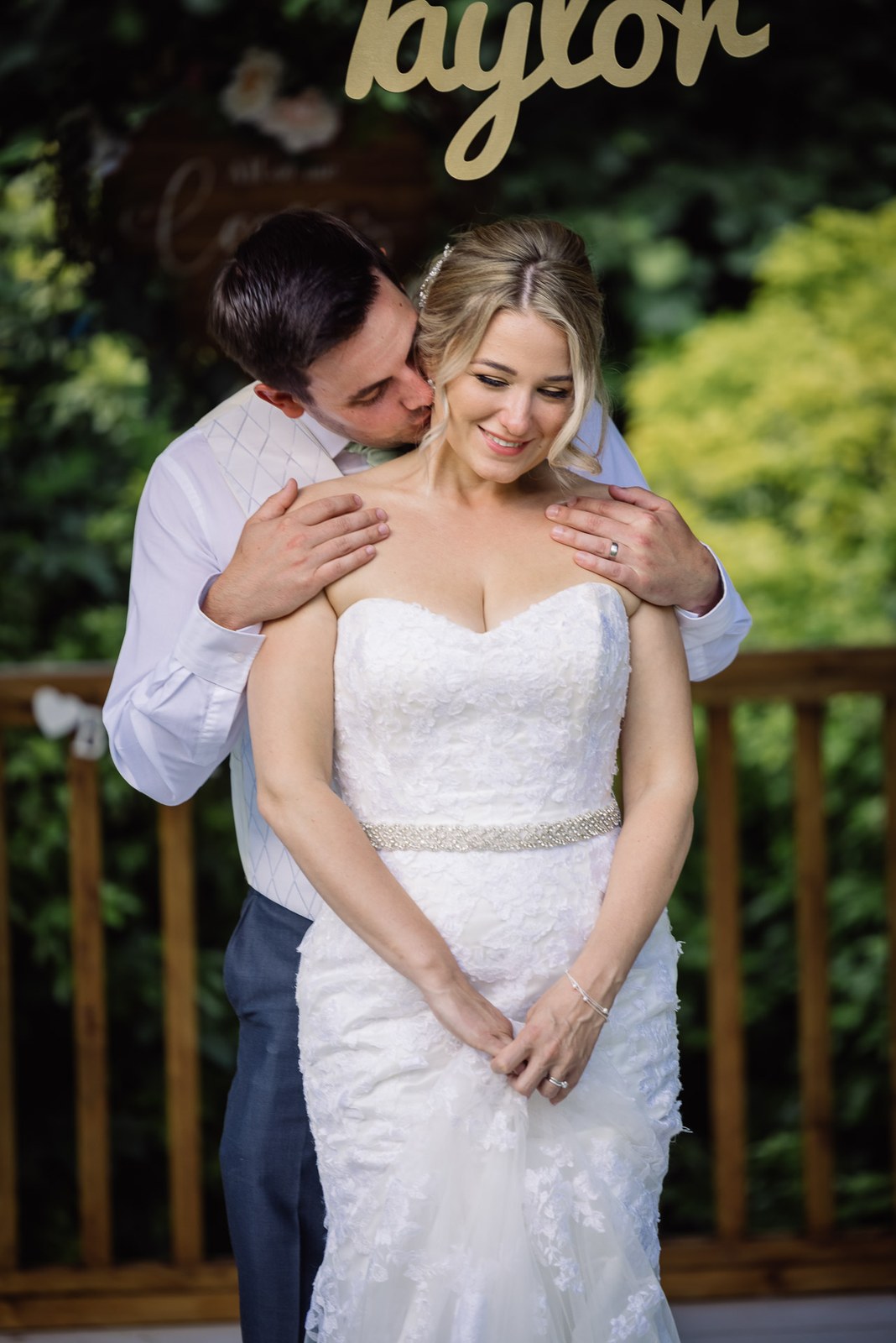 The groom kissing the bride's cheek beneath a gold script name sign