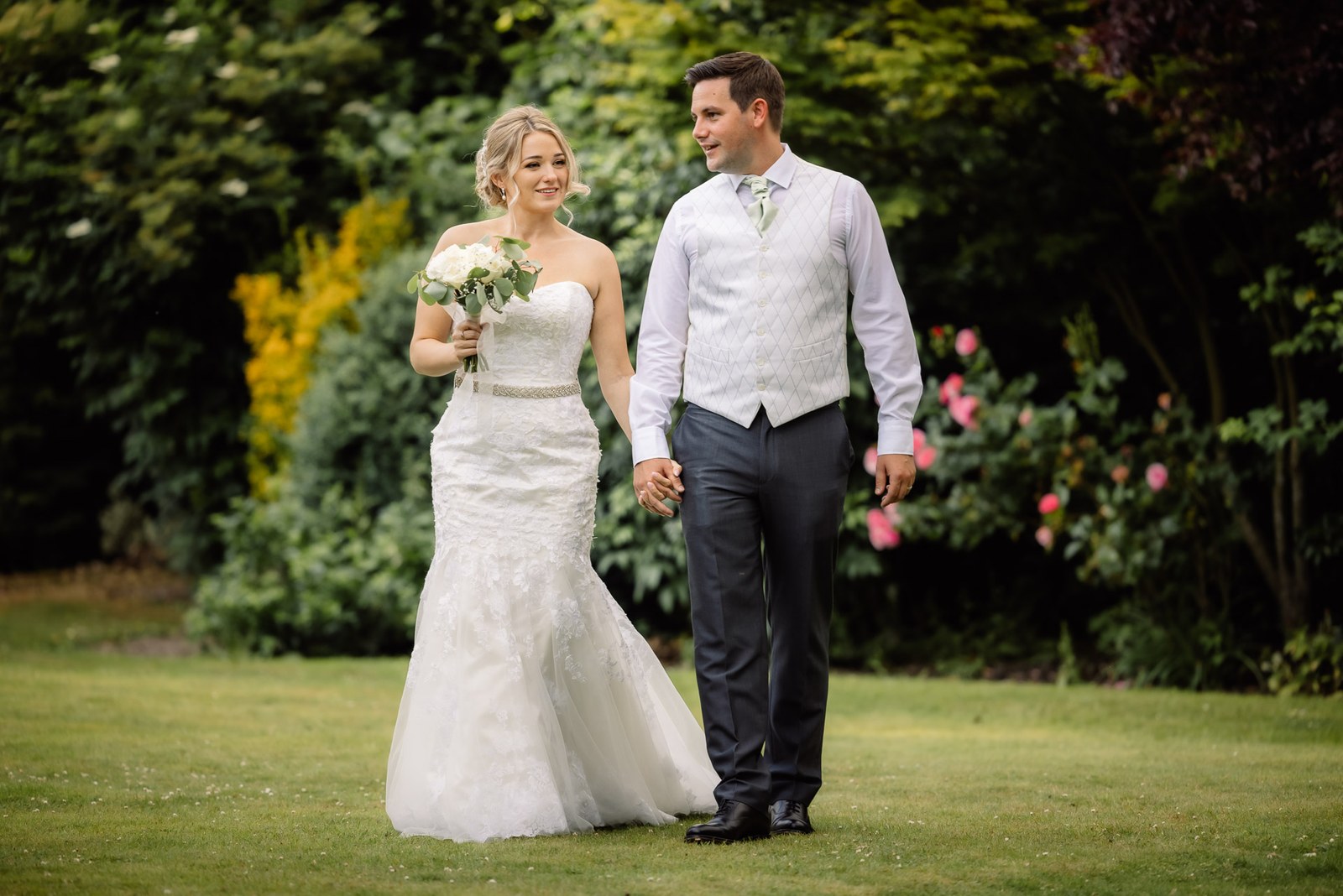 Bride and groom strolling hand in hand across the garden