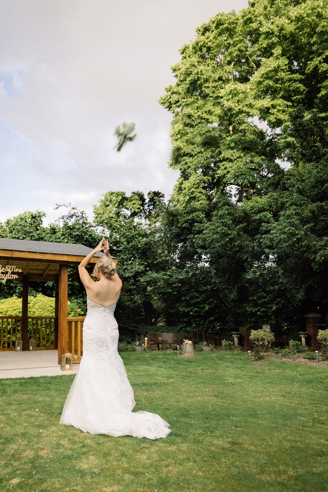 The bride tossing her bouquet on the lawn by the wooden gazebo