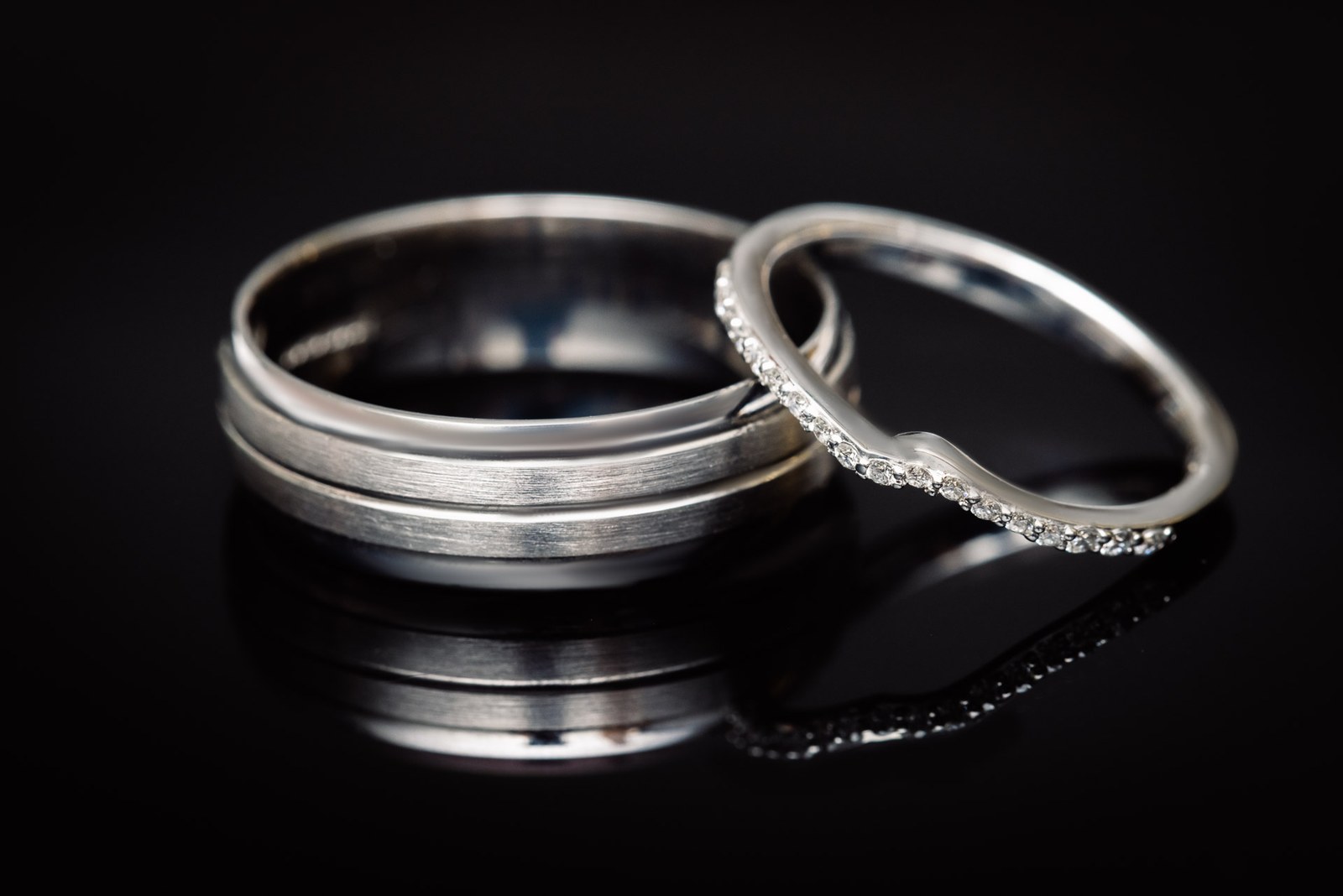Close-up of the wedding bands, one plain and one diamond-set, on black
