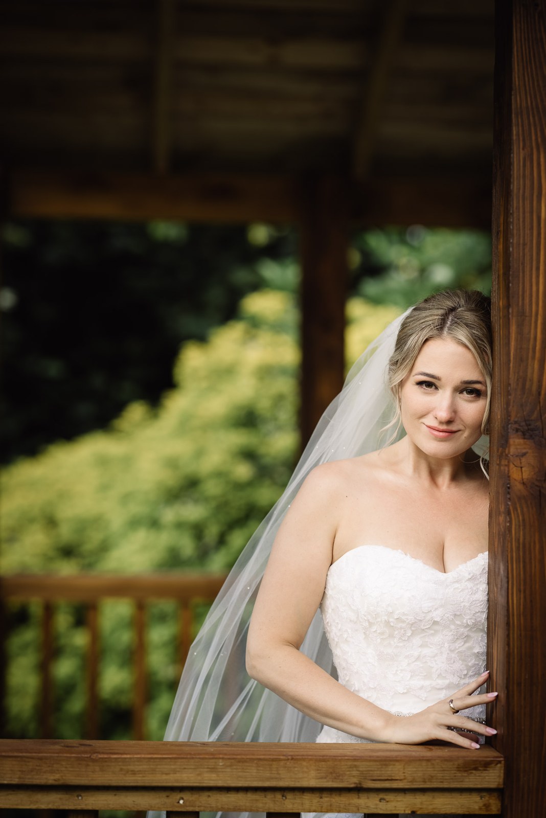 The bride leaning against the timber post of the garden gazebo
