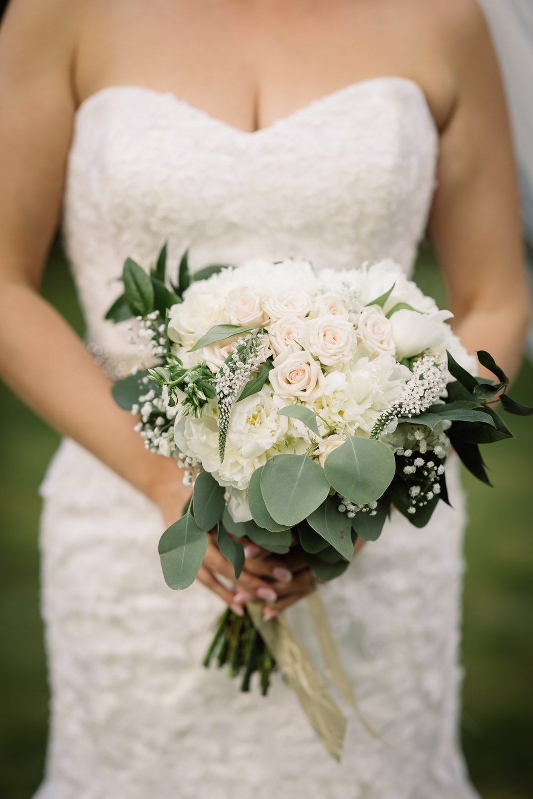 The bride's strapless gown and white rose bouquet in close detail