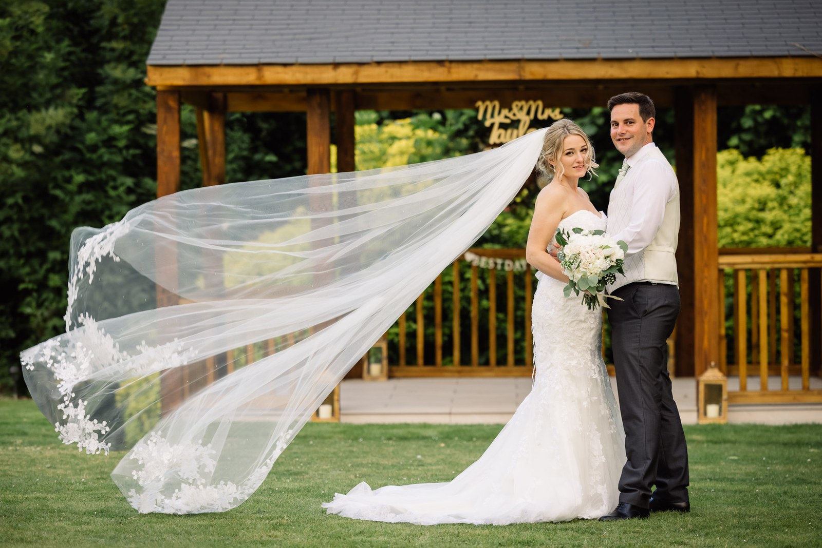 Bride and groom by the gazebo, her long veil streaming in the breeze