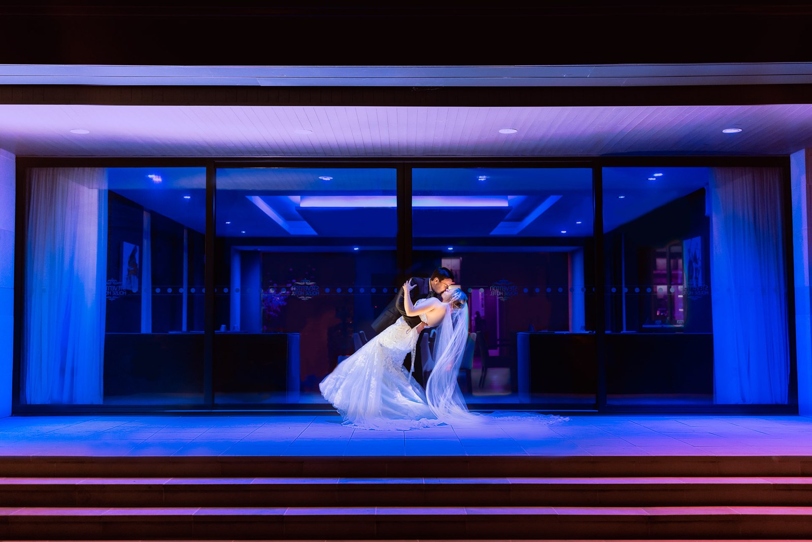 Bride and groom kissing in a dramatic blue-lit dip after dark at Steventon House Hotel