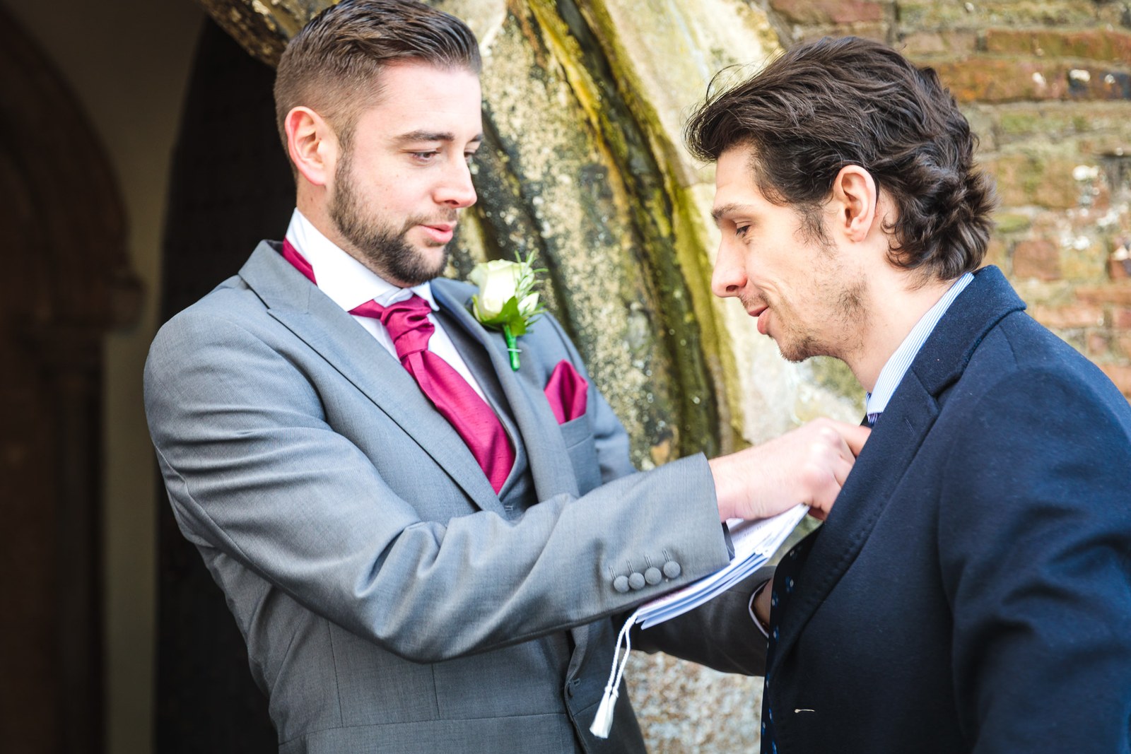 A groomsman pins a buttonhole onto a guest by the church doorway