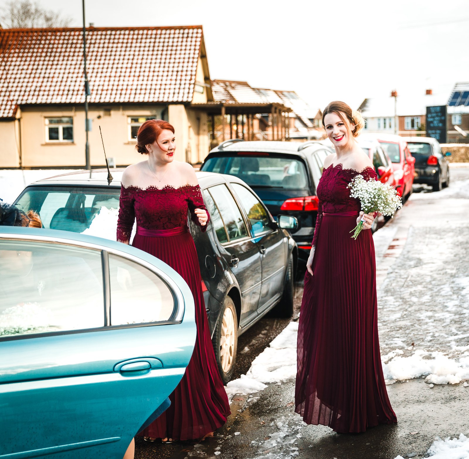 Two bridesmaids in burgundy climb from the car with a bouquet amid the snow