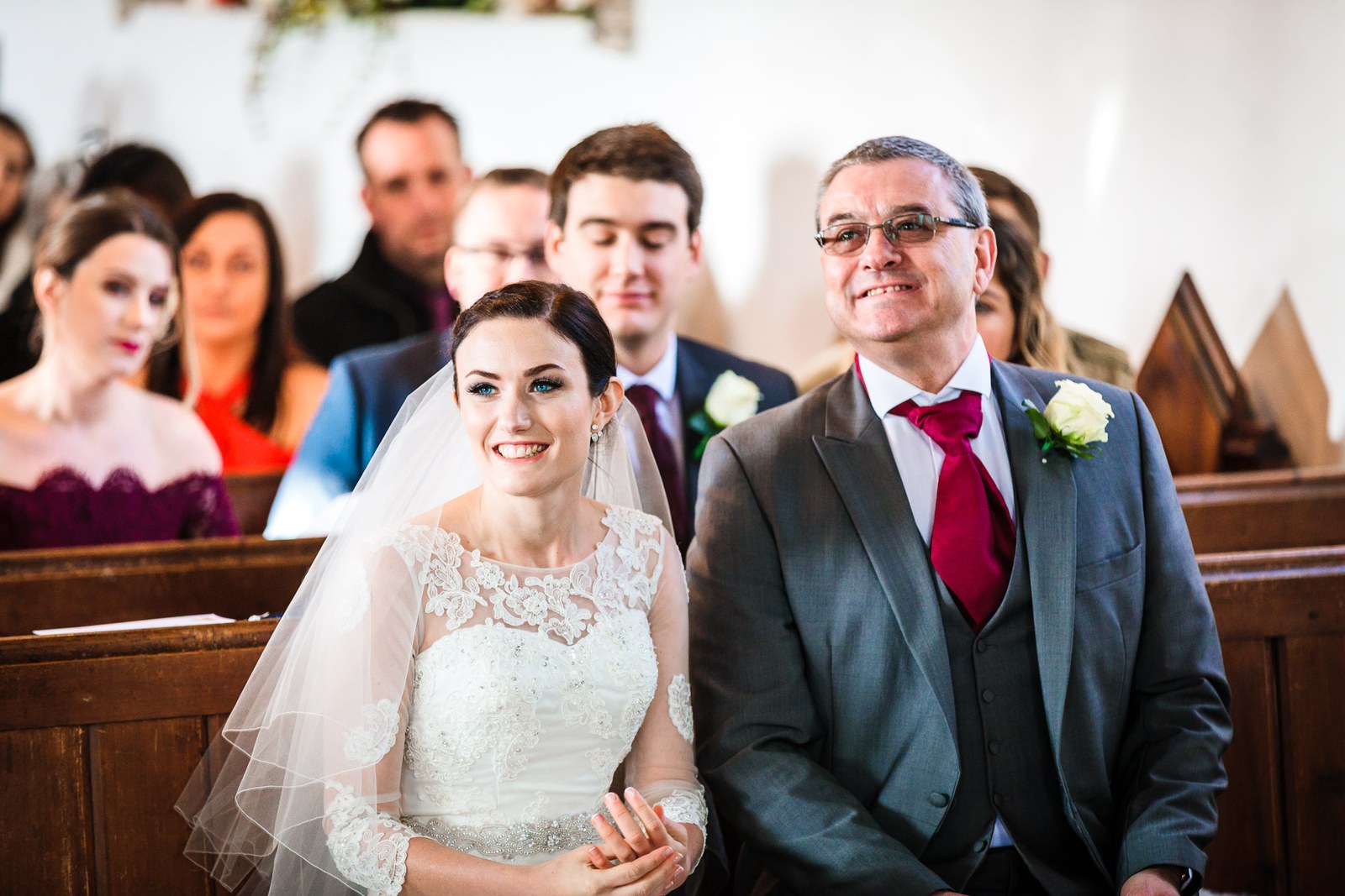 Father of the bride smiles beside her as guests look on from the pews