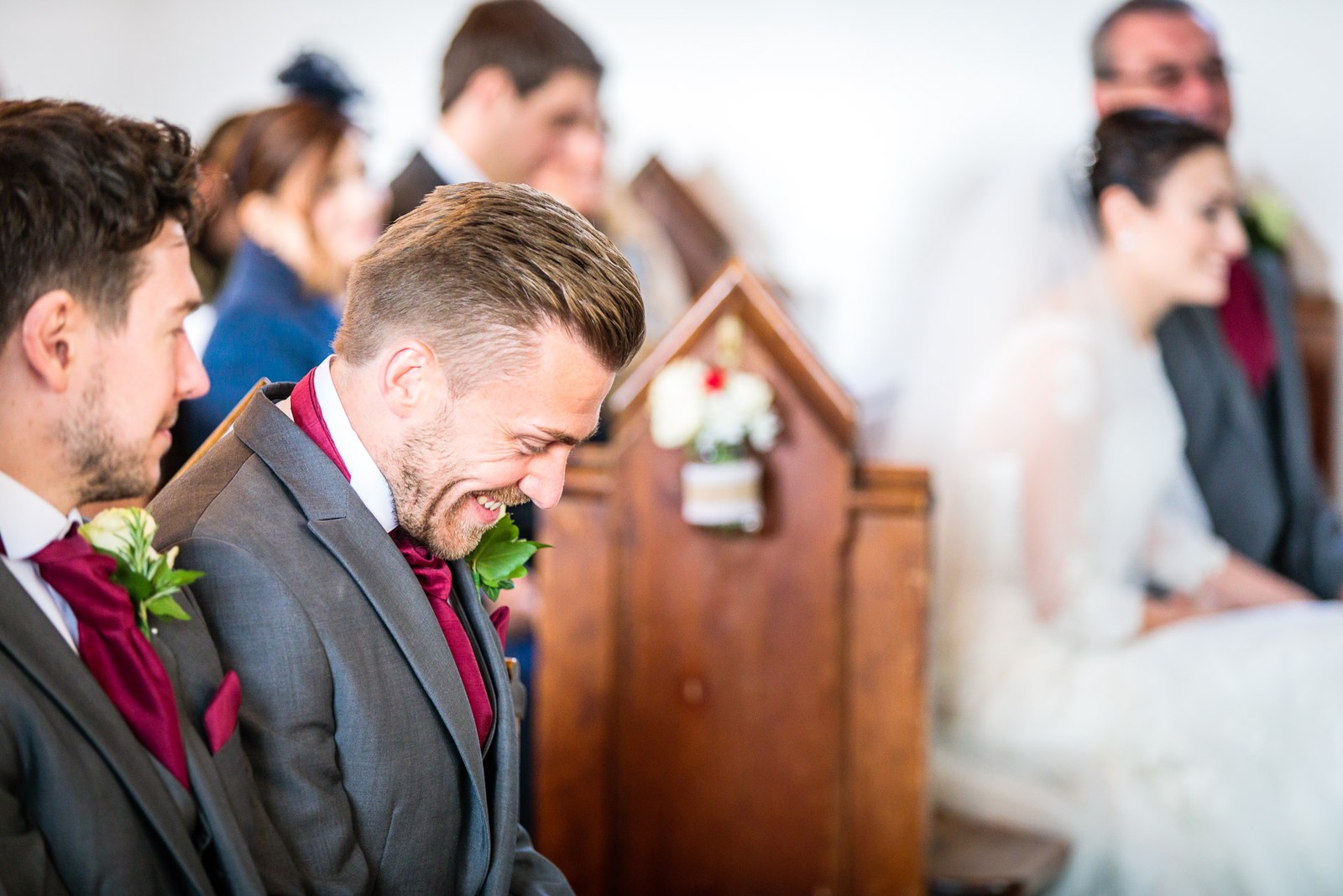 The groom and best man share a laugh in the pew as the bride watches