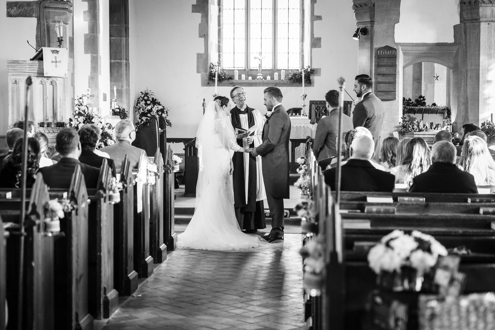 Black and white aisle view of the couple at the altar in the church