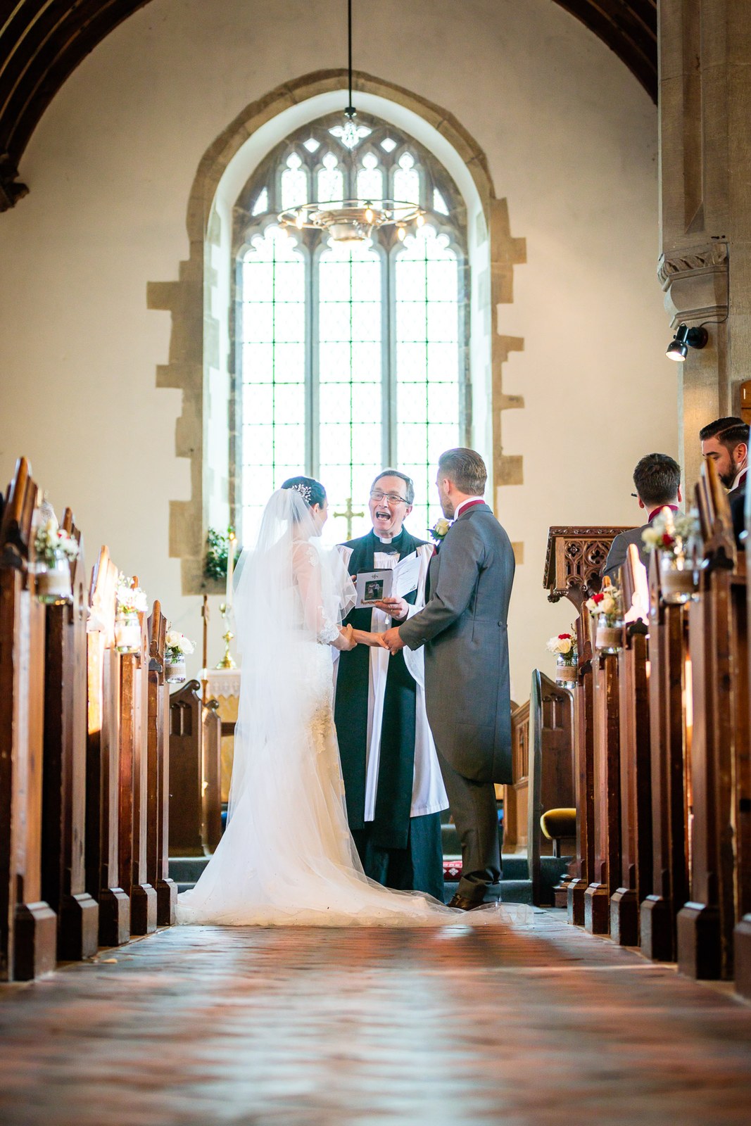 The couple stand at the altar beneath a tall arched church window