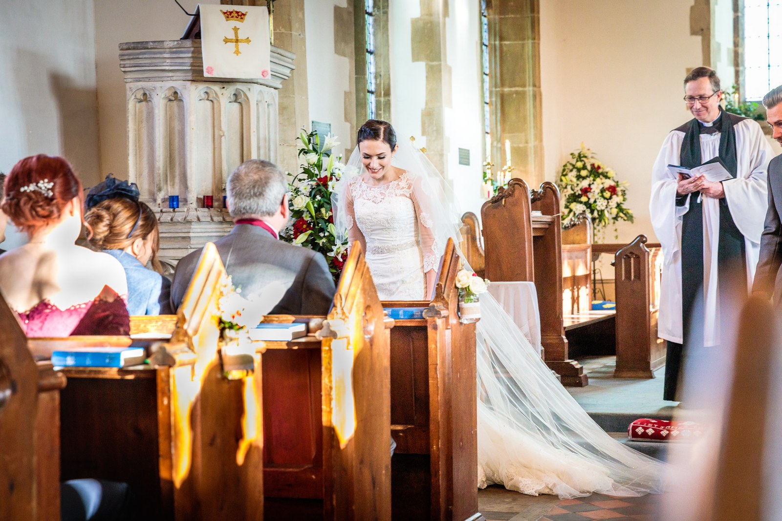 Bride stands in the church with her long train spread as the vicar reads